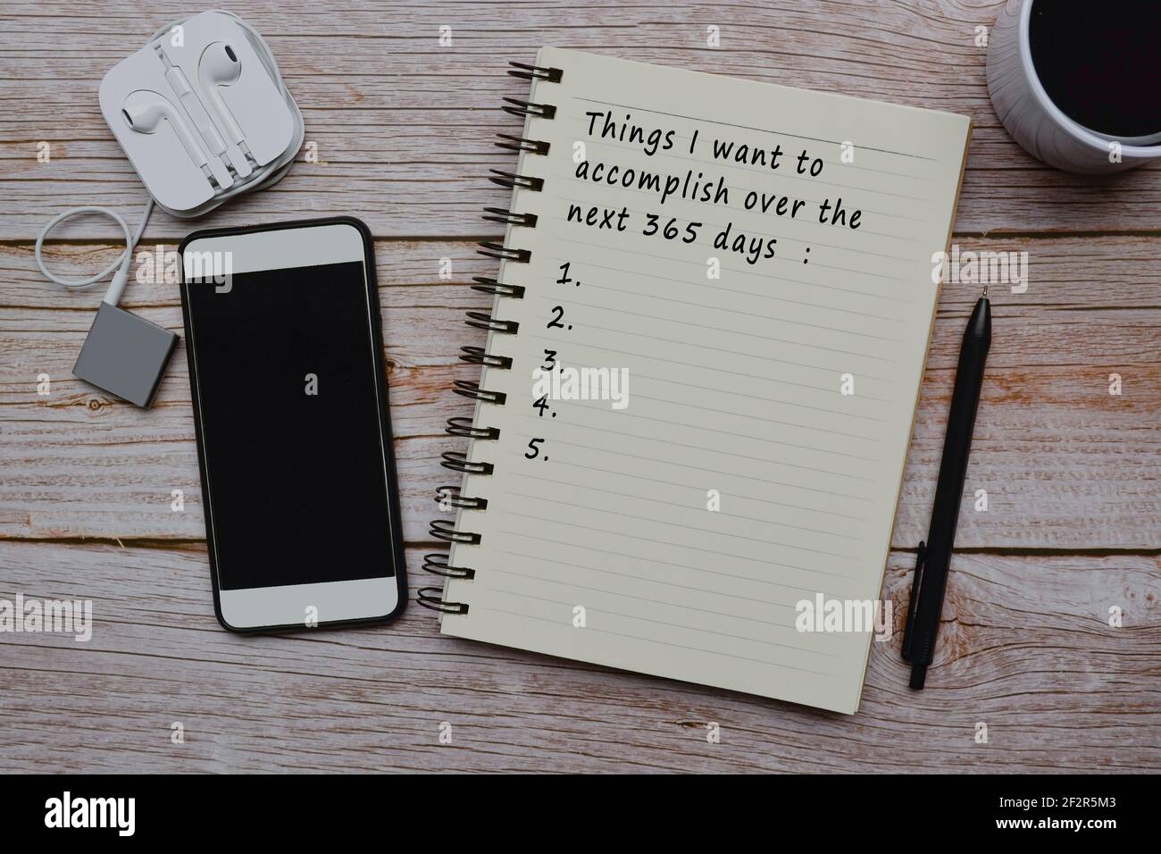 Text auf Notizblock mit Tasse Kaffee, Smartphone, Musik-Player und Stift auf Holztisch - Dinge, die ich in den nächsten 365 Tagen erreichen möchte Stockfoto