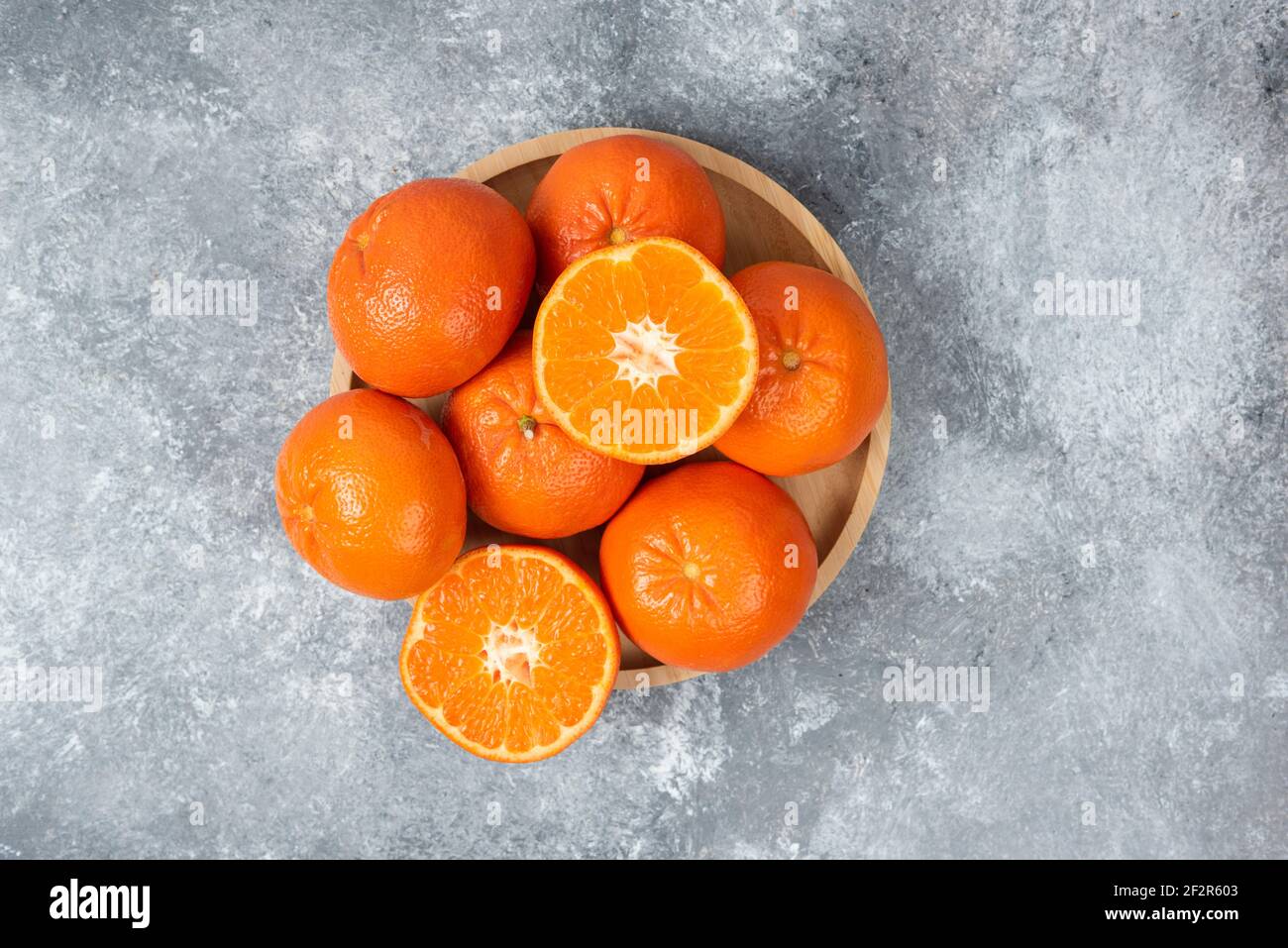 Saftige orange Früchte mit Scheiben in einem Holzteller auf Steinhintergrund Stockfoto