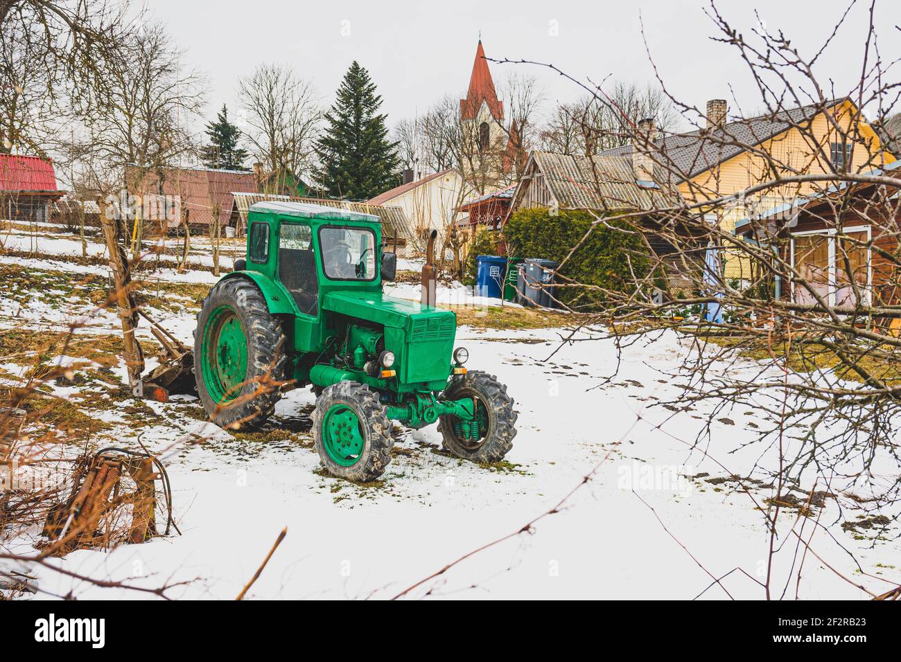 Typisches Holzhaus auf dem Land mit alten grünen Traktor Weißrussland im Garten im Winter, mit Schnee. Belarus ist eine Serie von vierrädrigen Traktor Stockfoto