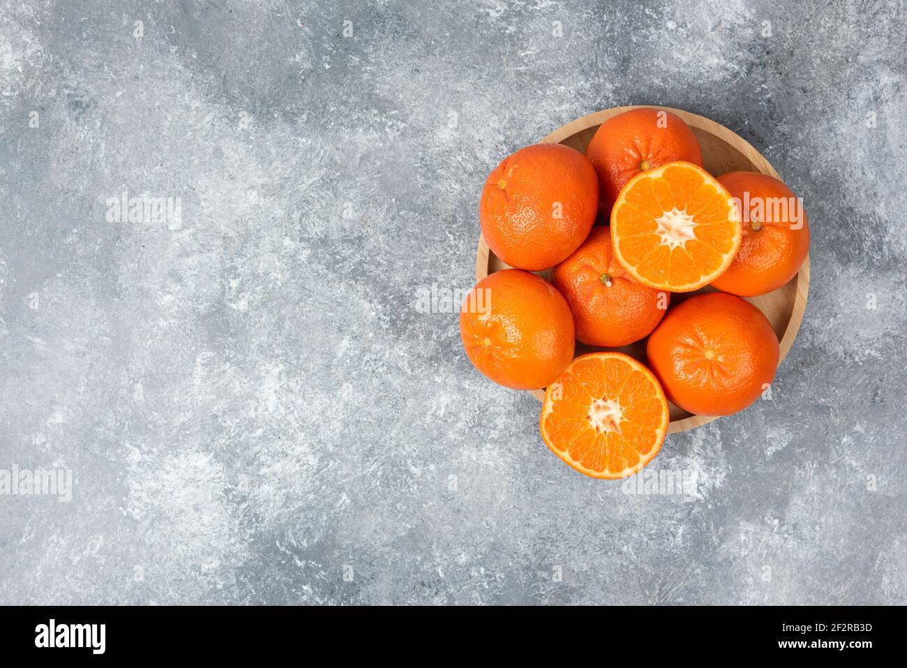 Saftige orange Früchte mit Scheiben in einem Holzteller auf Steinhintergrund Stockfoto
