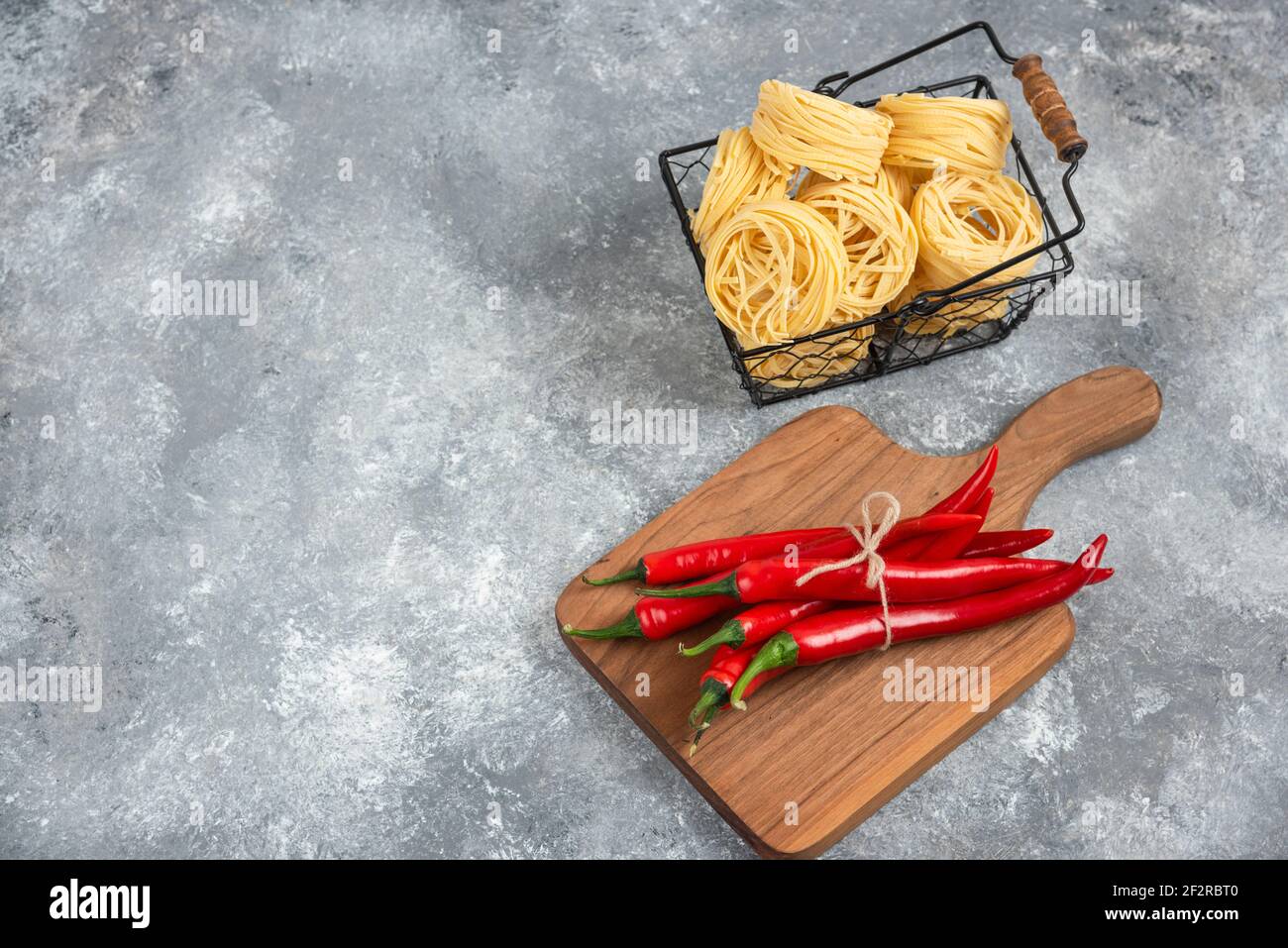 Korb mit rohen Nudeln und Chilischoten auf Marmoroberfläche Stockfoto