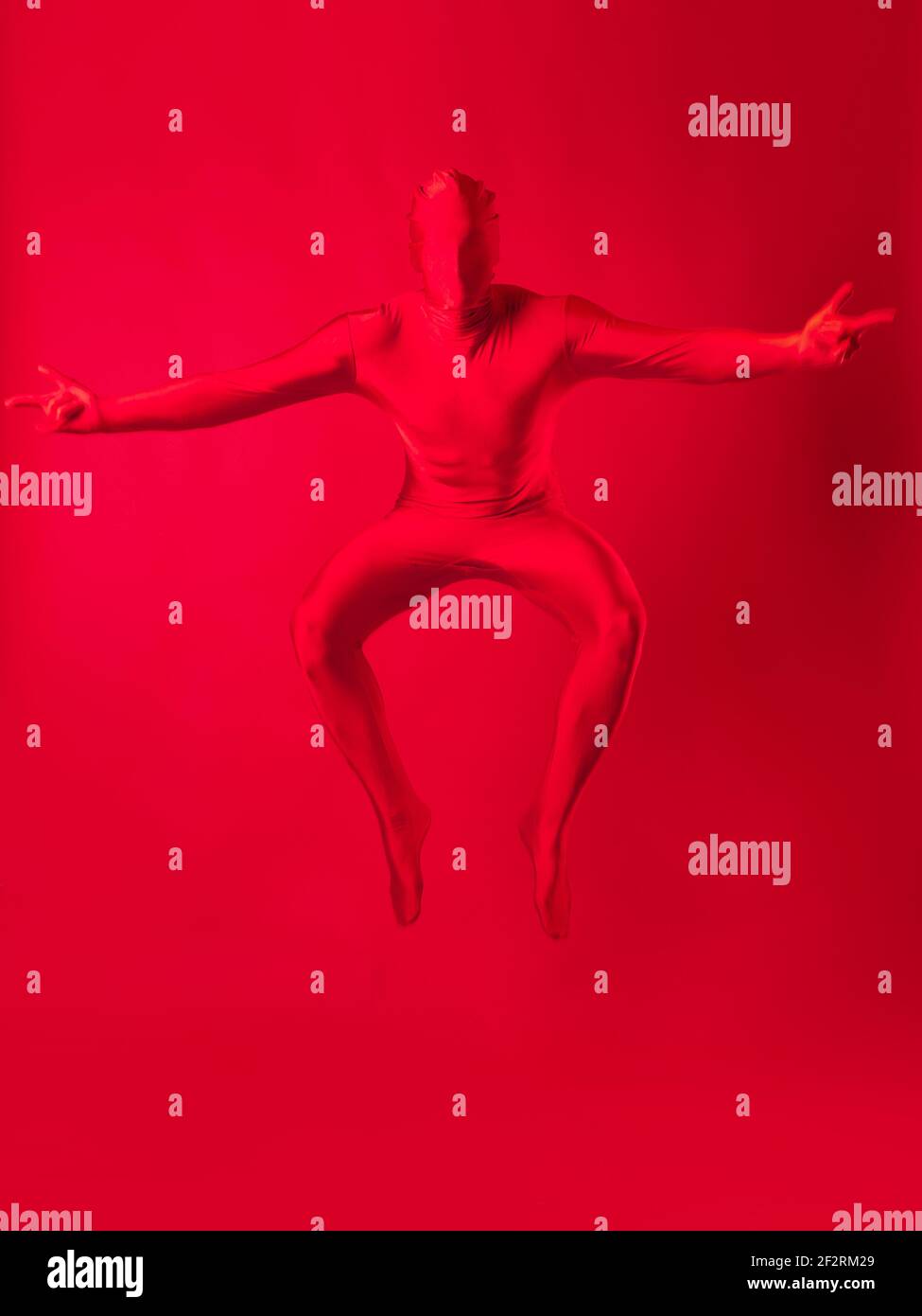 Verrückter roter Mann auf rotem Hintergrund. Figur in einem Trikot, das den ganzen Körper bedeckt und Gesicht springt auf. Stockfoto