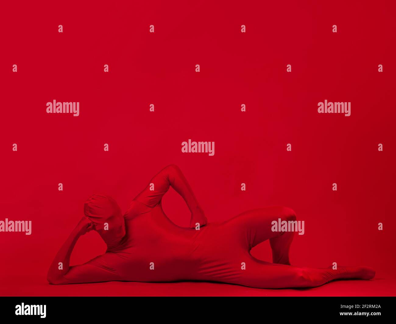 Verrückter roter Mann auf rotem Hintergrund, Figur in einem Trikot, das den ganzen Körper und das Gesicht bedeckt, das auf dem Boden liegt. Stockfoto