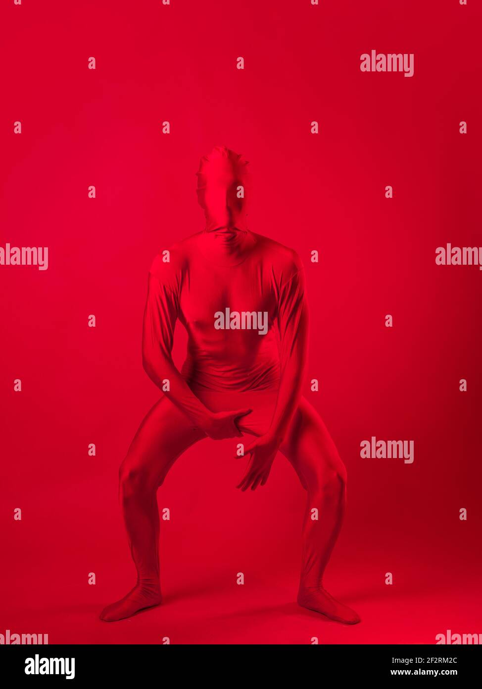 Verrückter roter Mann auf rotem Hintergrund. Figur in einem Trikot, das den ganzen Körper und das Gesicht bedeckt. Stockfoto