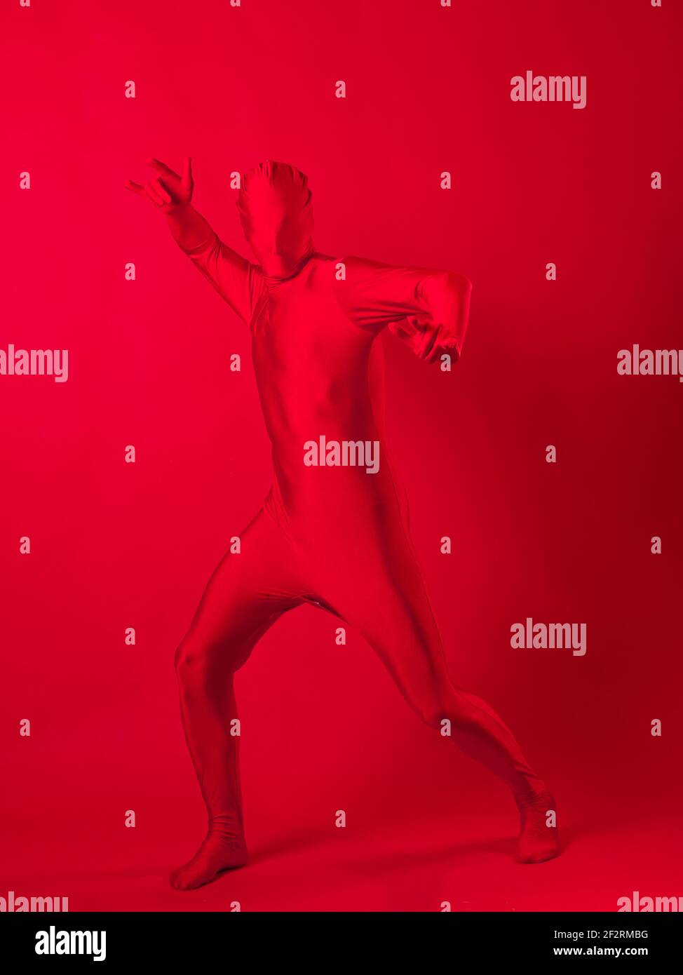 Verrückter roter Mann auf rotem Hintergrund. Figur in einem Trikot, das den ganzen Körper und das Gesicht bedeckt. Stockfoto