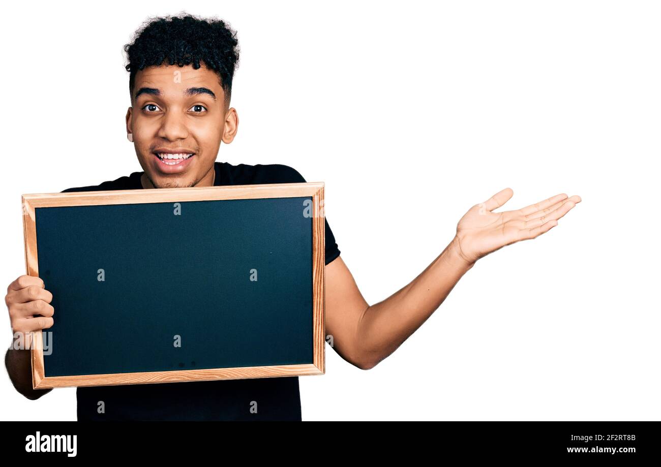 Junger afroamerikanischer Mann mit Tafel feiert Sieg mit glücklich Lächeln und Ausdruck des Gewinners mit erhobenen Händen Stockfoto