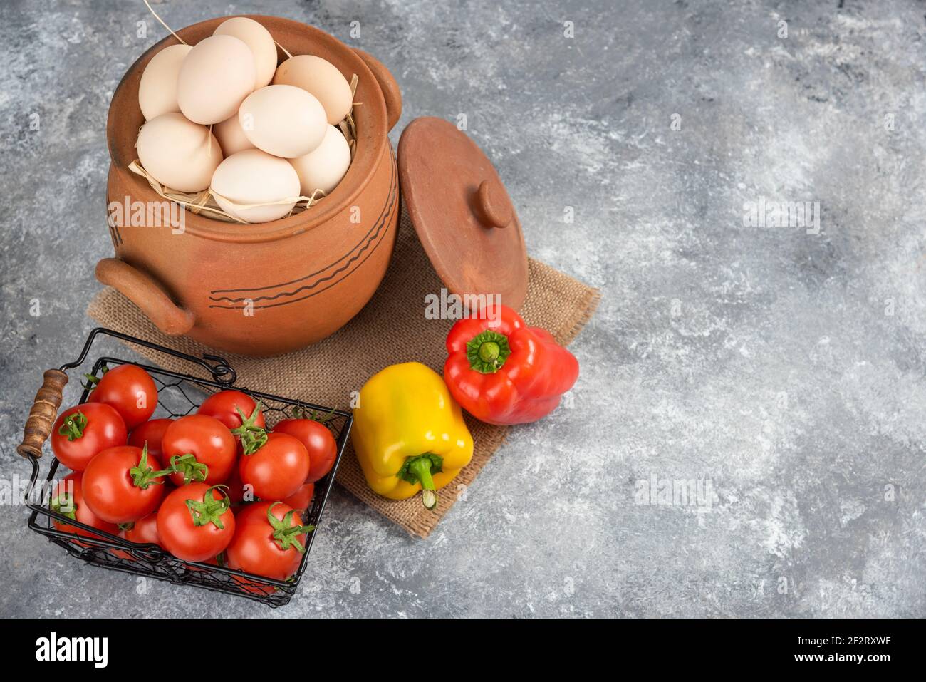 Topf mit rohen Eiern, Tomaten und Paprika auf Marmor Hintergrund Stockfoto