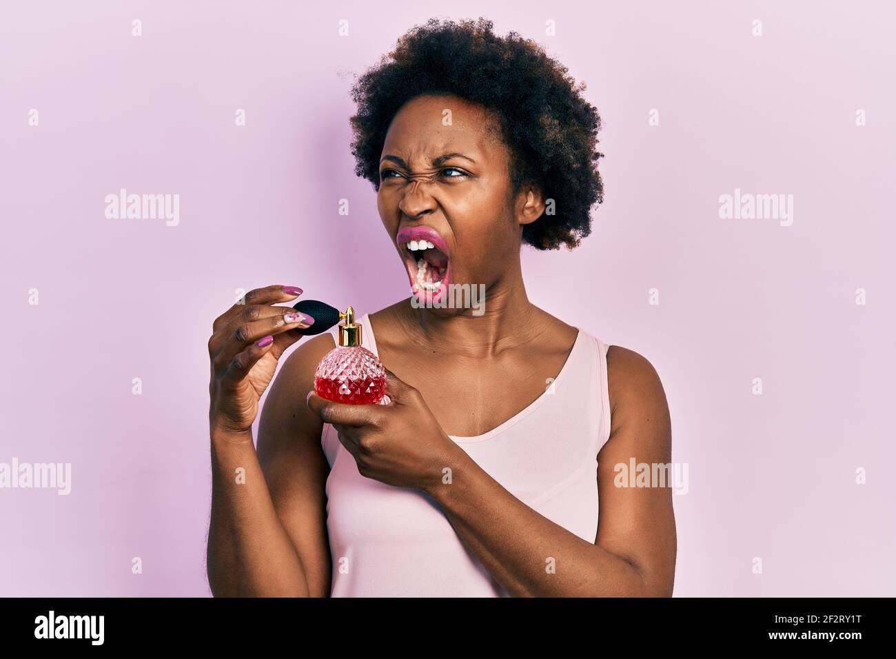 Junge afroamerikanische Frau hält Parfüm wütend und verrückt schreien frustriert und wütend, schreien vor Wut. Wut und aggressive Konzept. Stockfoto