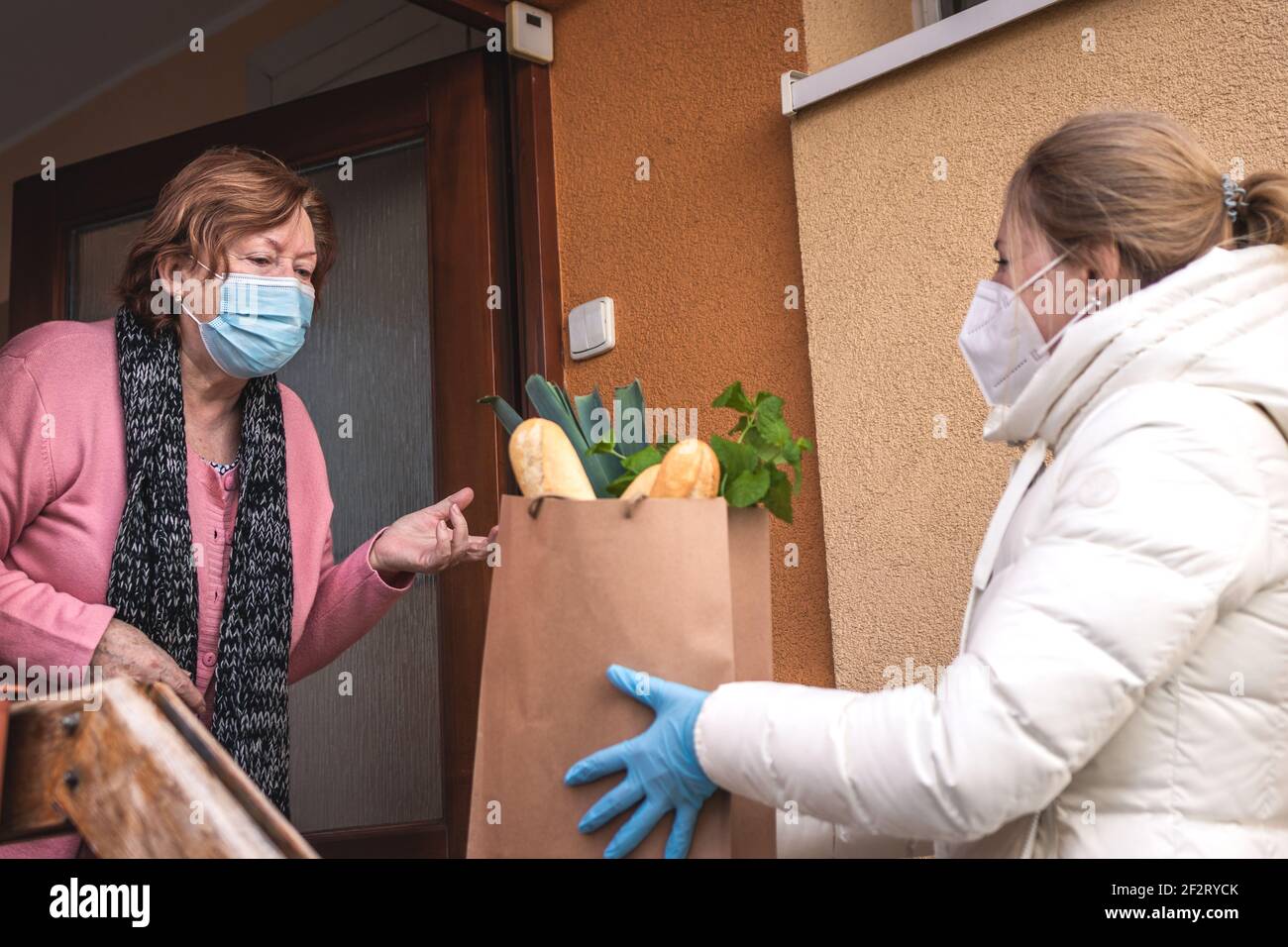 Hilfe beim Einkauf von Lebensmitteln während des Pandemieausbruchs. Volunteer trägt FFP2 Maske während der Lieferung von Lebensmitteln an ältere Frau. Support-Community Stockfoto