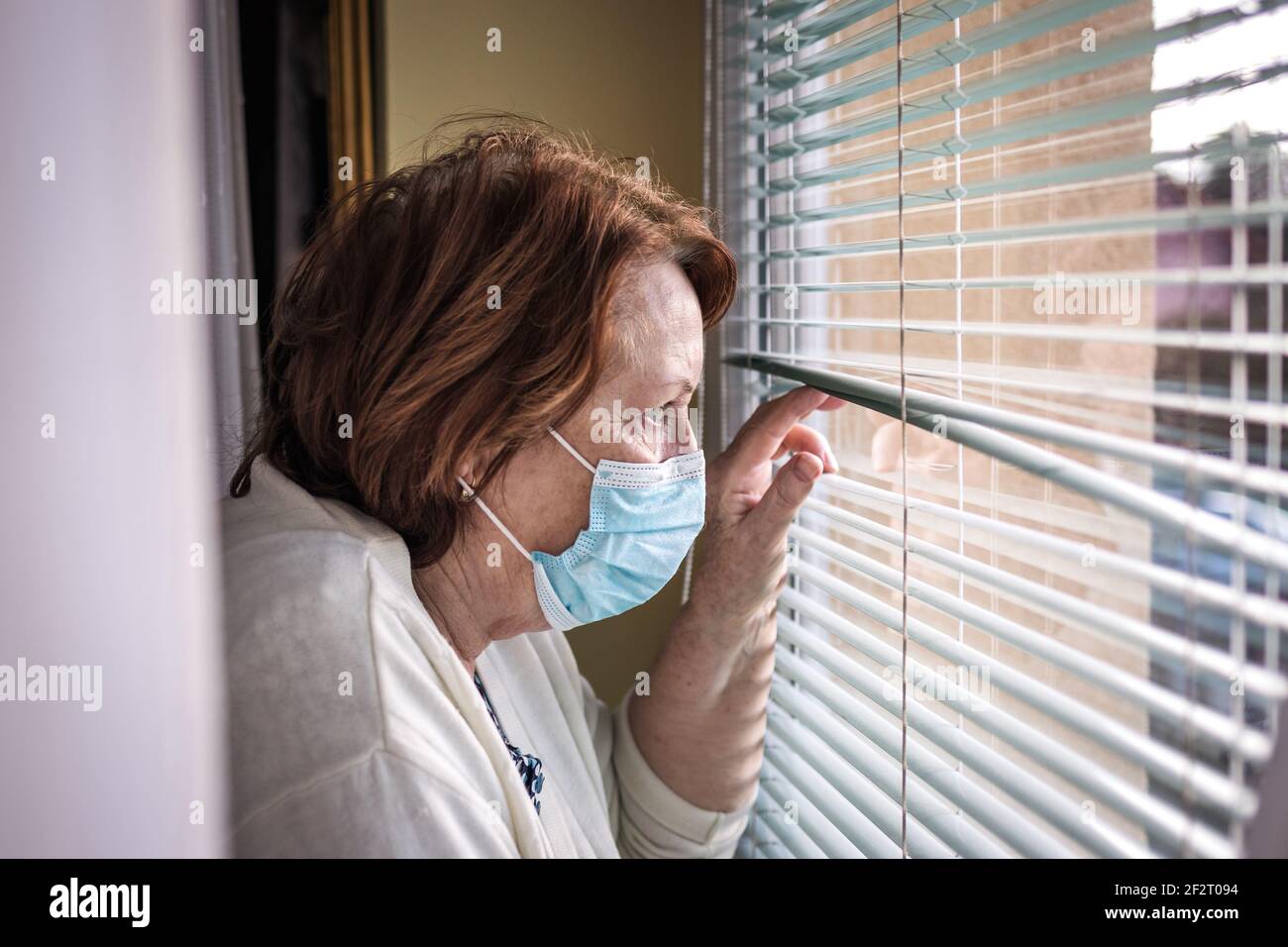 Einsame traurige ältere Frau mit Gesichtsmaske, die durch das Fenster schaut Während der covid-19 Pandemie Quarantäne und Sperrung Stockfoto