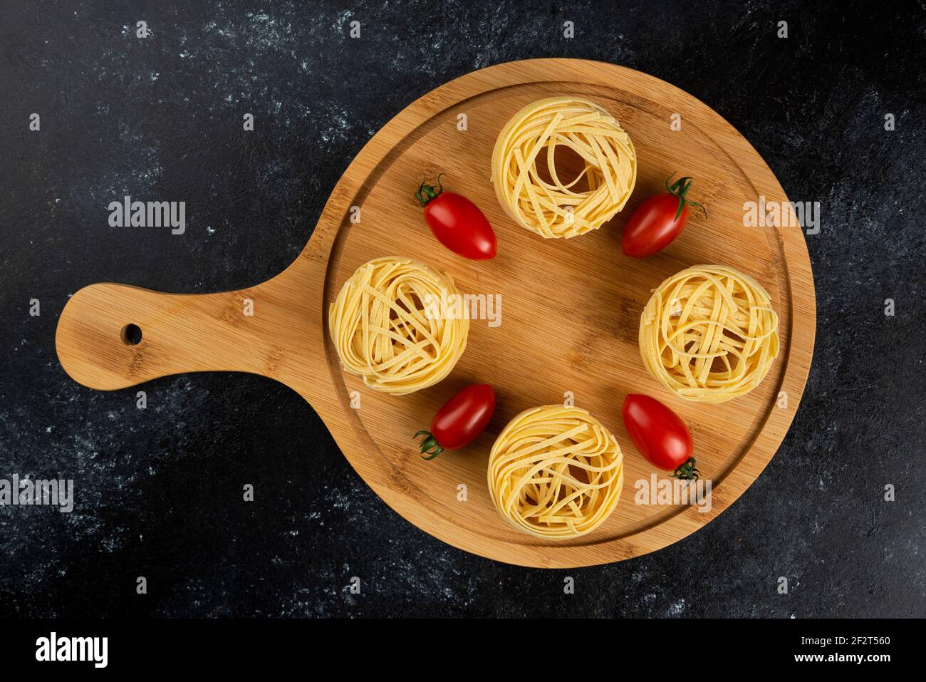 Ungekochte Nudelnester und Tomaten auf Holzbrett Stockfoto