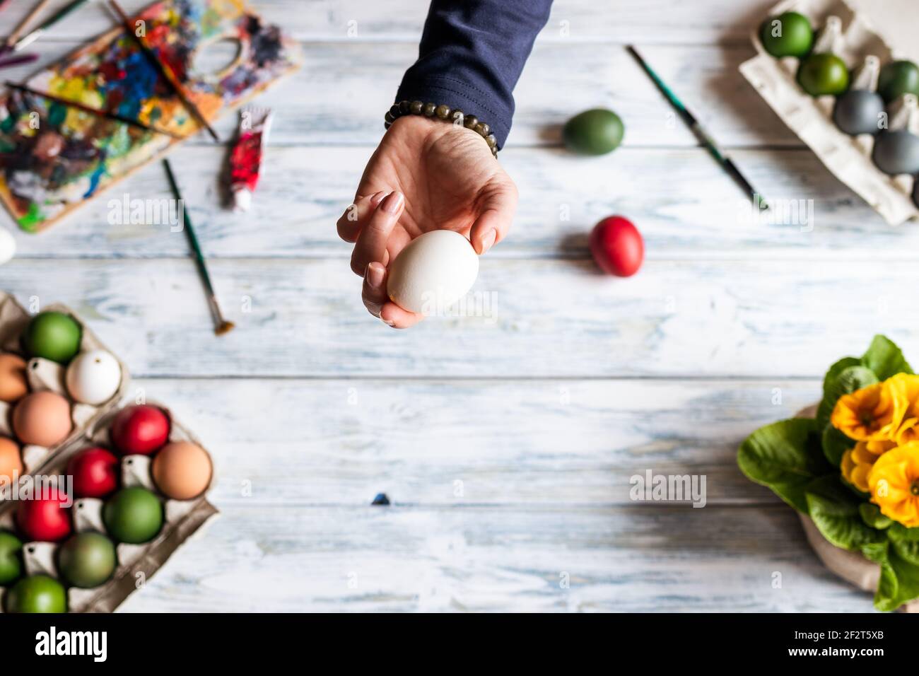 Frau hält weißes Ei in der Hand über dem Tisch. Malen und Dekorieren Ostereier Stockfoto
