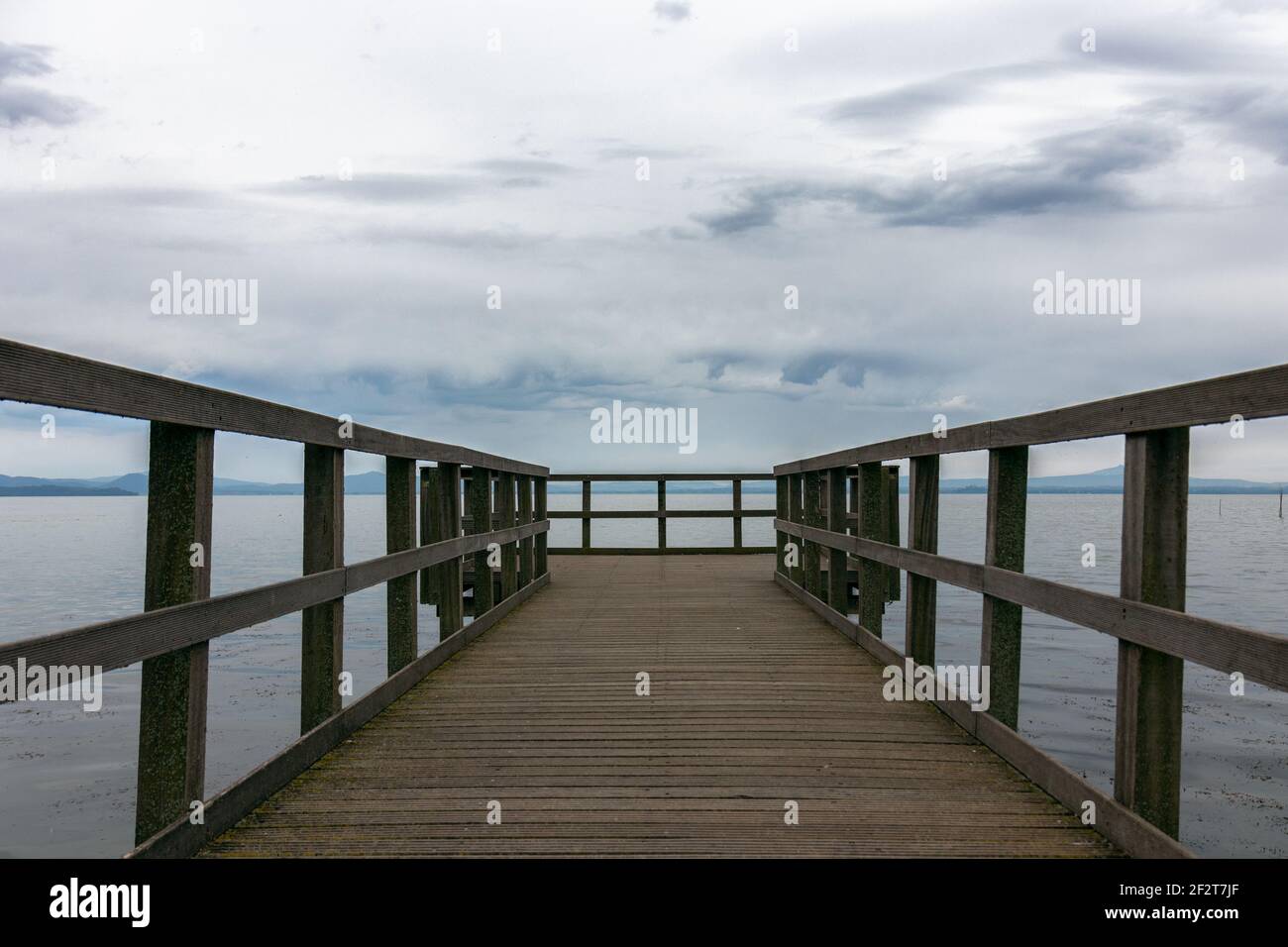 Schöne Aussicht auf den Trasimenischen See vom Pier aus. Der Himmel ist bedeckt und ruhiges Wasser, keine Menschen. Nostalgische Stimmung. Umbrien, Italien Stockfoto