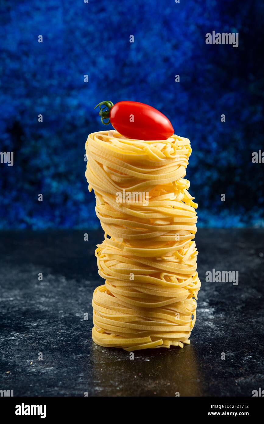 Ungekochte Nudelnester und Tomaten auf Marmortisch Stockfoto
