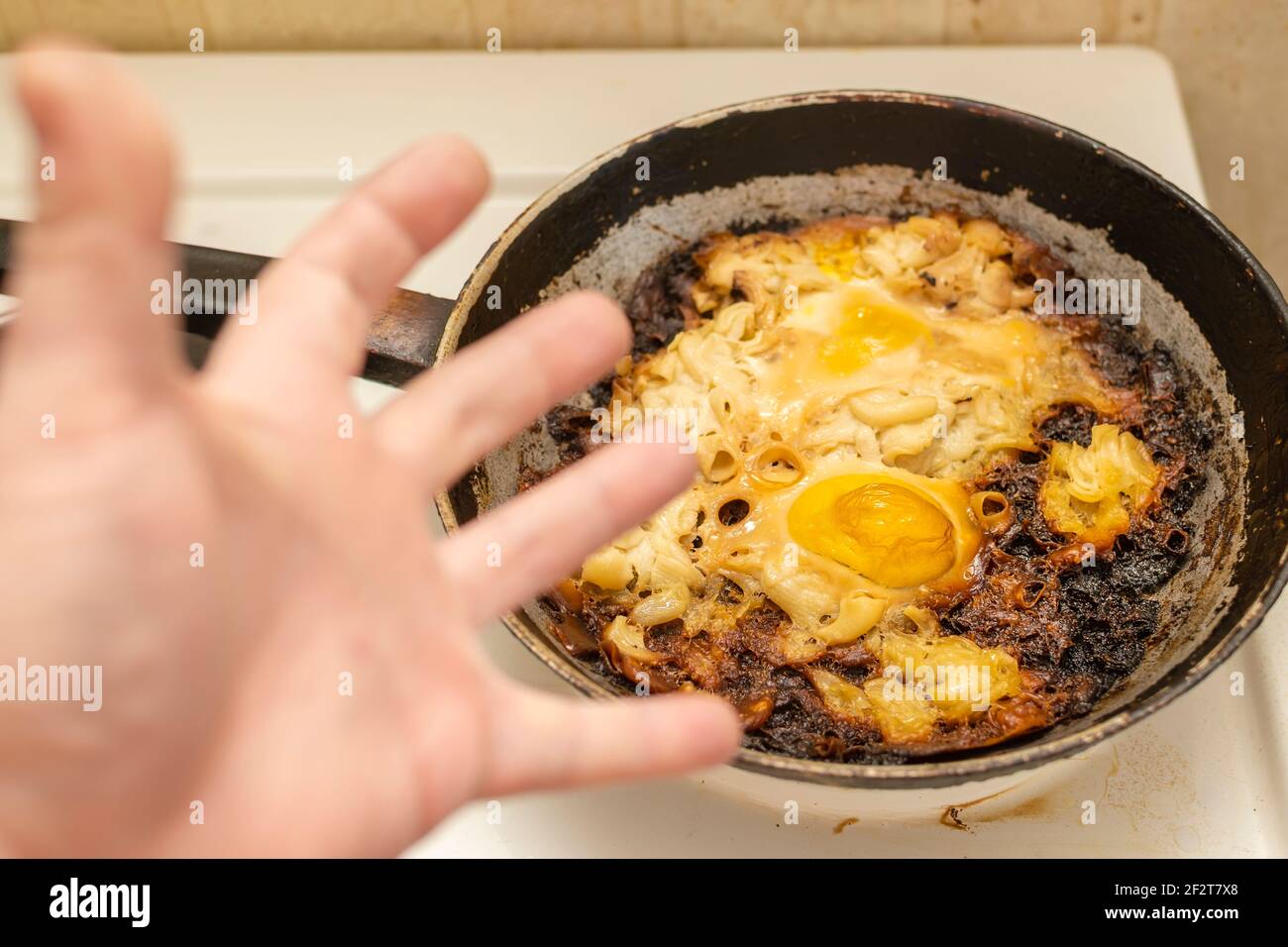 Blick auf verkochte, verbrannte Eier, Omelette auf einer alten gusseisernen Pfanne auf einem Elektroherd vor dem Hintergrund der Hand Stockfoto