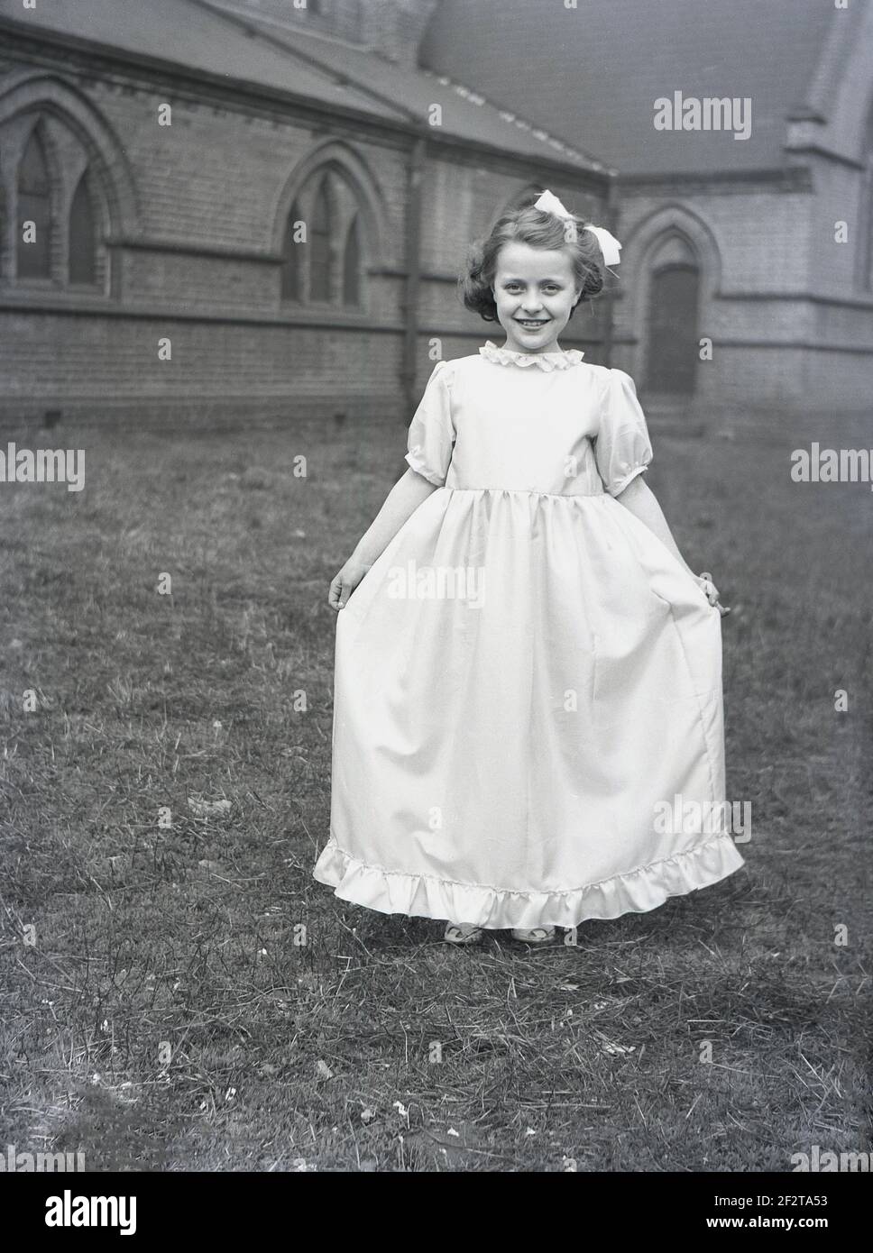 1956, historisch, ein hübsches junges Mädchen auf dem Gelände einer Kirche, das ihr Kleid für die traditionelle Frühlingsparade oder den Karneval vorführt, Leeds, England, Großbritannien. Stockfoto