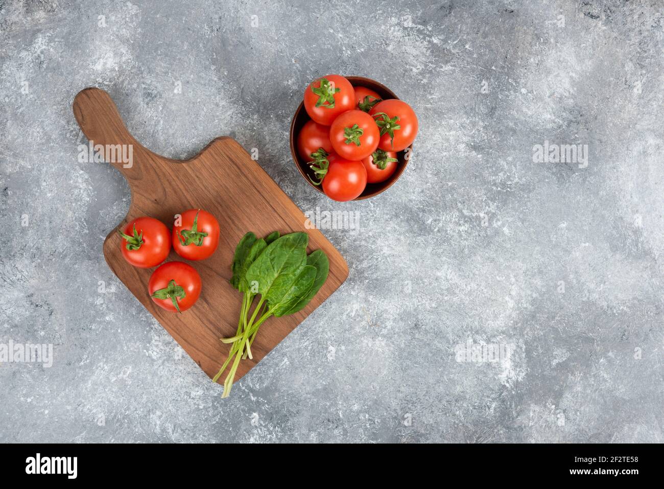 Holzschüssel mit roten Tomaten mit Grüntönen auf Marmorboden Stockfoto