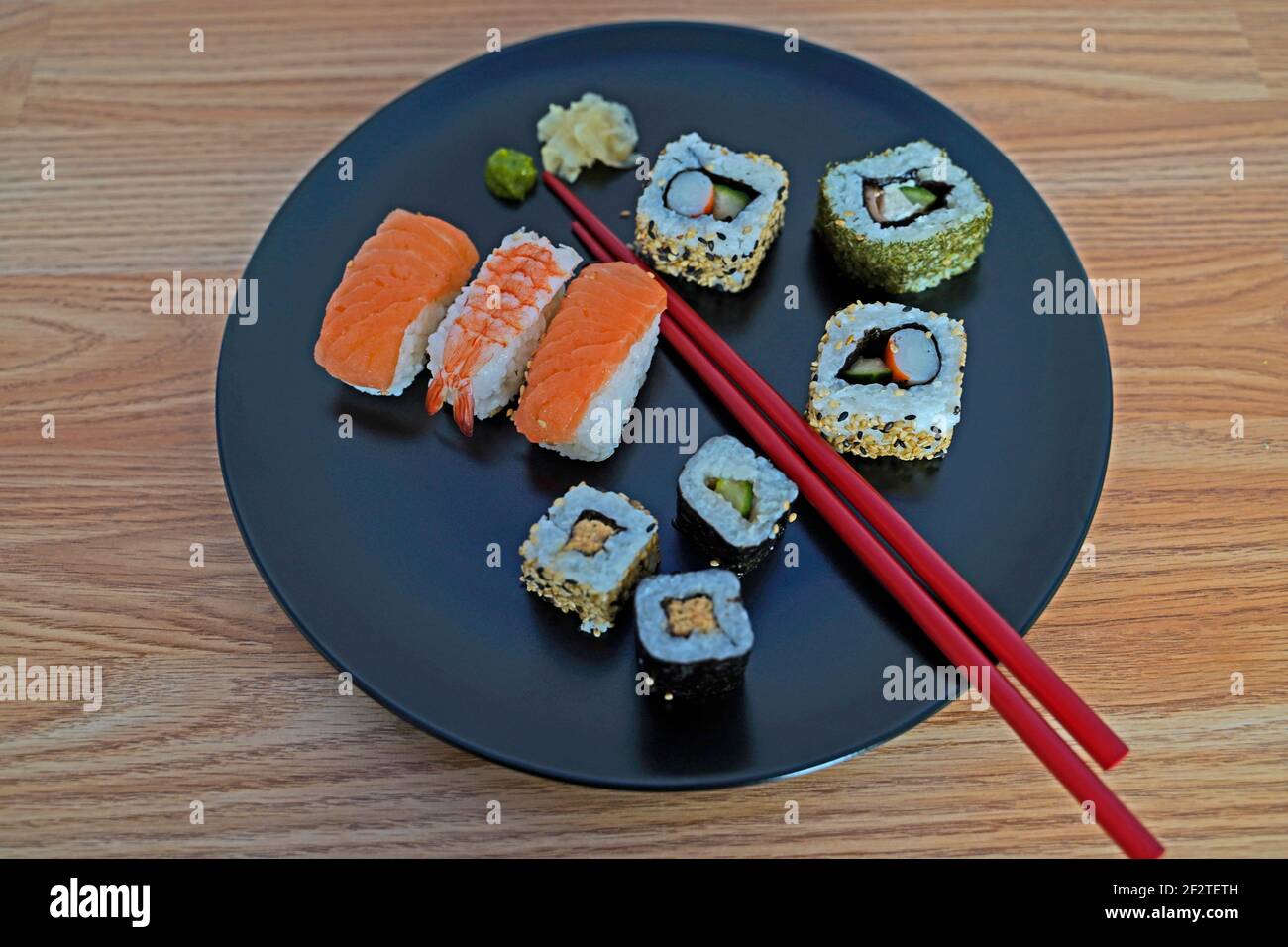 Sushi auf einem schwarzen Teller mit Essstäbchen arrangiert Stockfoto