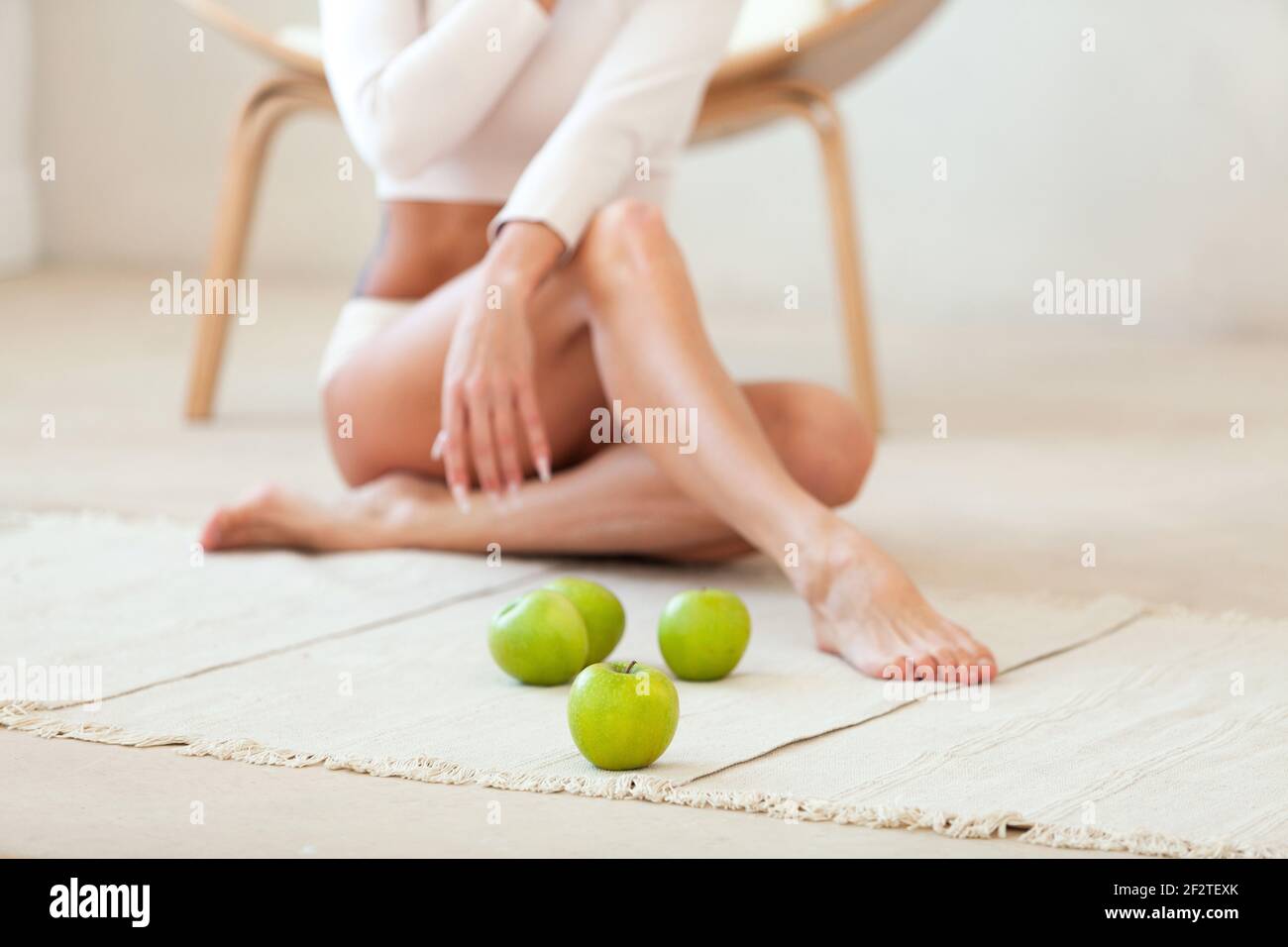 Frau mit langen Beinen sitzt auf dem Boden mit grünen Äpfeln. Der Fokus liegt auf dem nächsten Apfel. Gesunde Ernährung Konzept Stockfoto