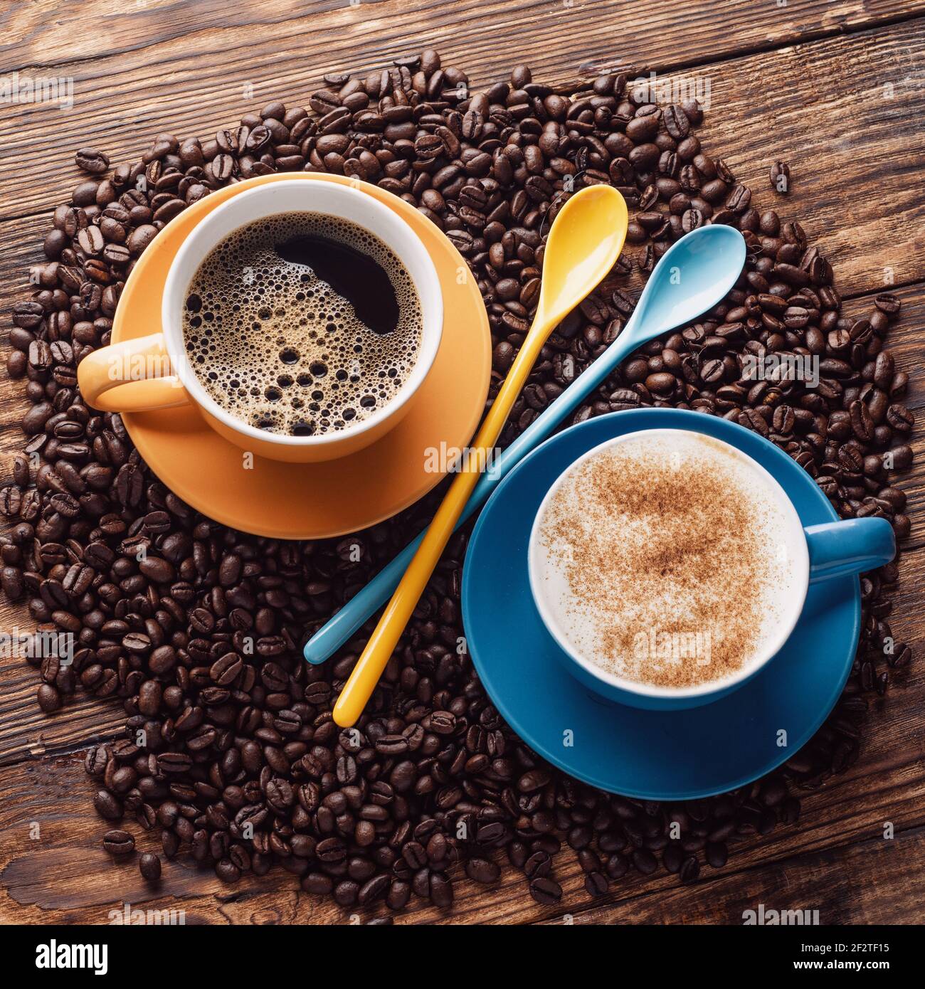 Blaue und gelbe Tassen Kaffee, Löffel, Bohnen auf einem Holzbackgroun. Stockfoto