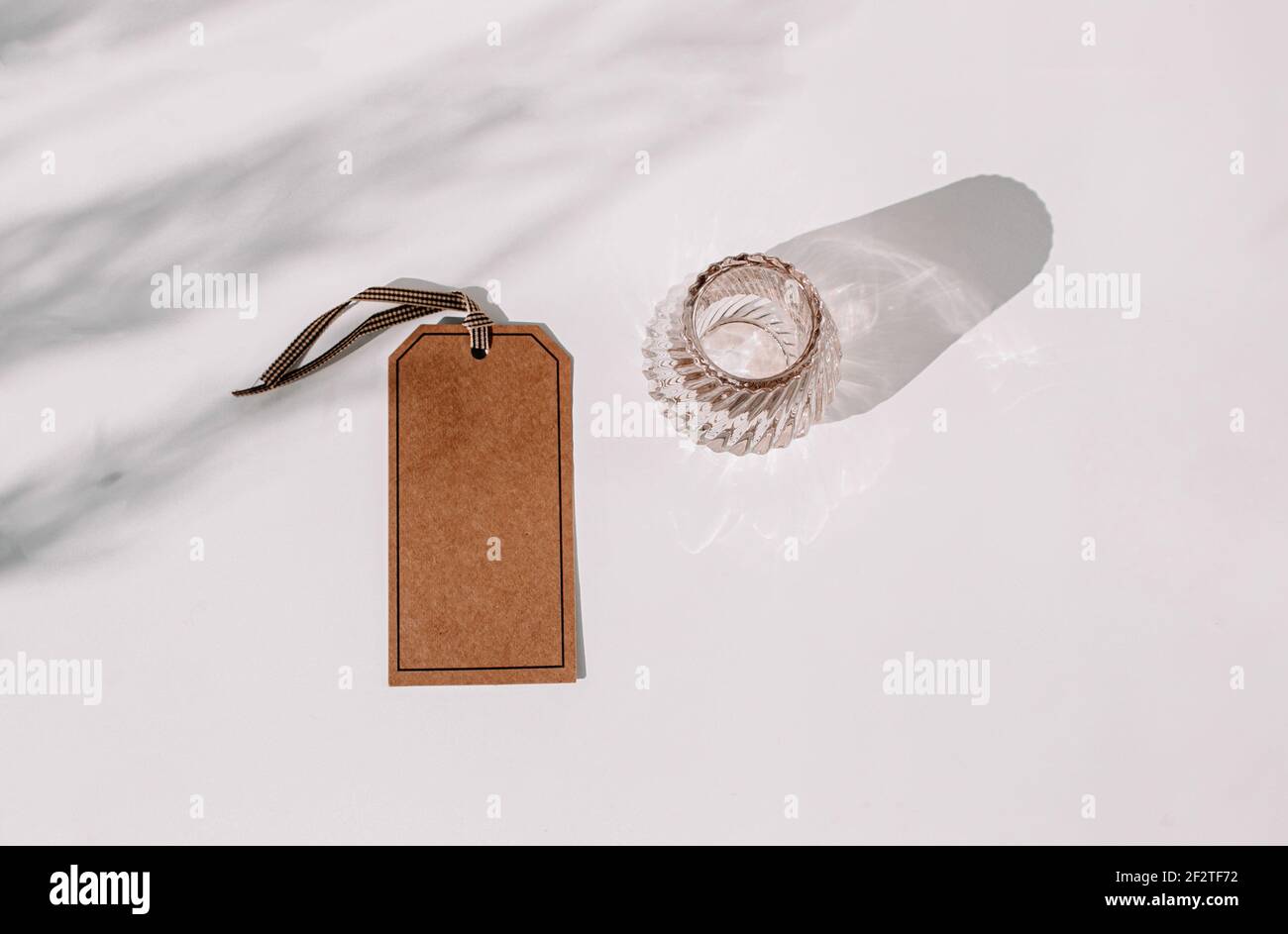 Braunes Etikett mit Glas auf einem weißen Tisch mit Schattierungen, fügen Sie einen Text auf einem Tag oder Ihr eigenes Design-Element hinzu Stockfoto