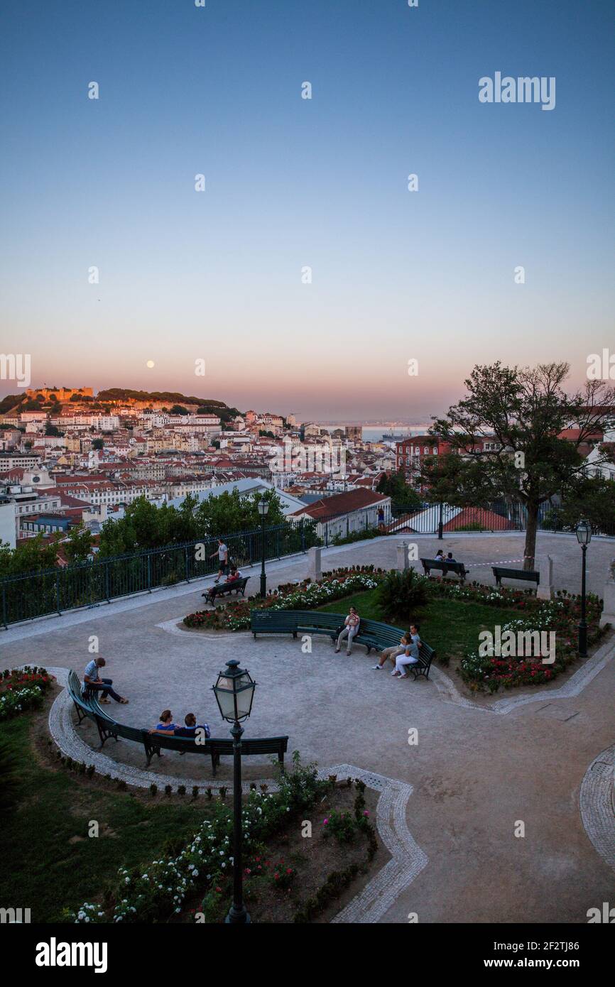 Touristen, die den Sonnenuntergang genießen und sich im Garten São Pedro de Alcântara entspannen, mit seinem Panoramablick auf das historische Zentrum von Lissabon, Portugal. Stockfoto