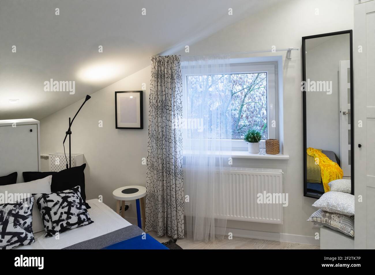 Ein Detail einer einrichtung im skandinavischen minimalistischen Stil. Ein kleines gemütliches Schlafzimmer mit einem Bett, einem Fenster und einem Spiegel in der Dachwohnung Stockfoto
