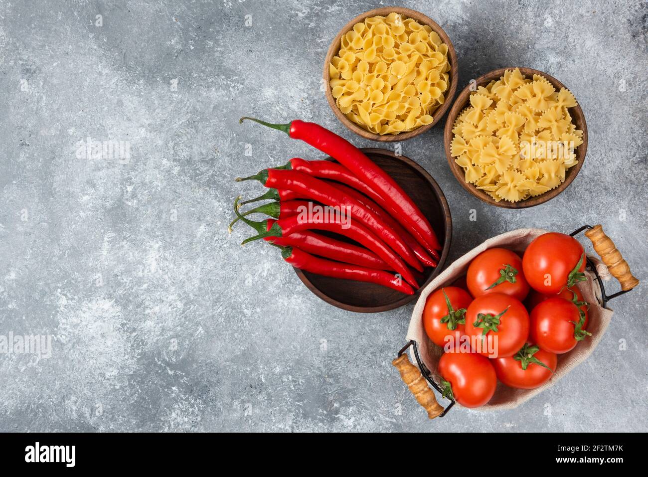 Holzschüsseln von roher Pasta mit roten Chilischoten und Tomaten Stockfoto