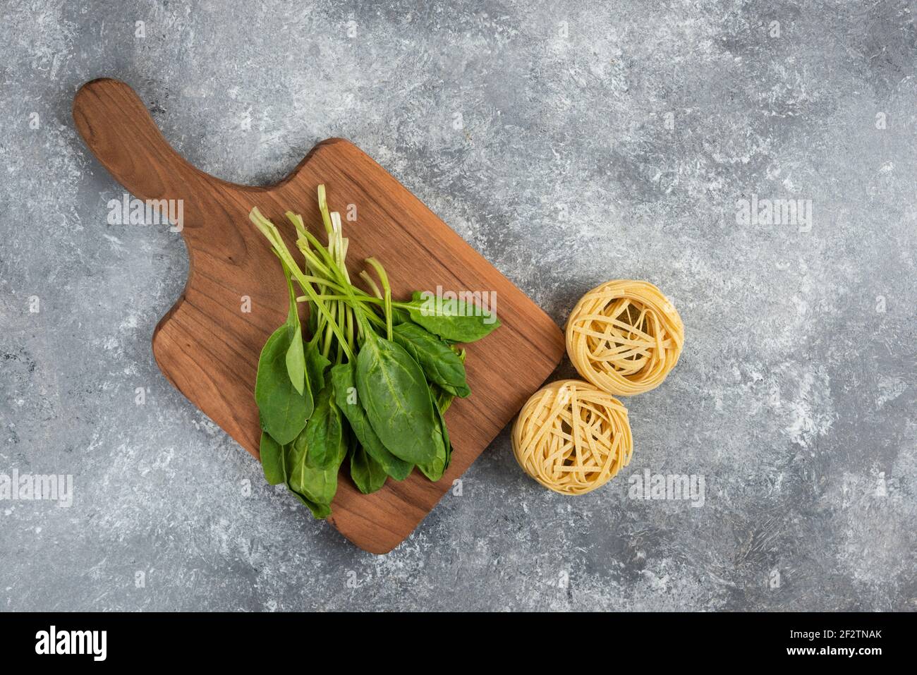 Rohe Nudelnester und gesunde grüne Blätter auf Marmoroberfläche Stockfoto
