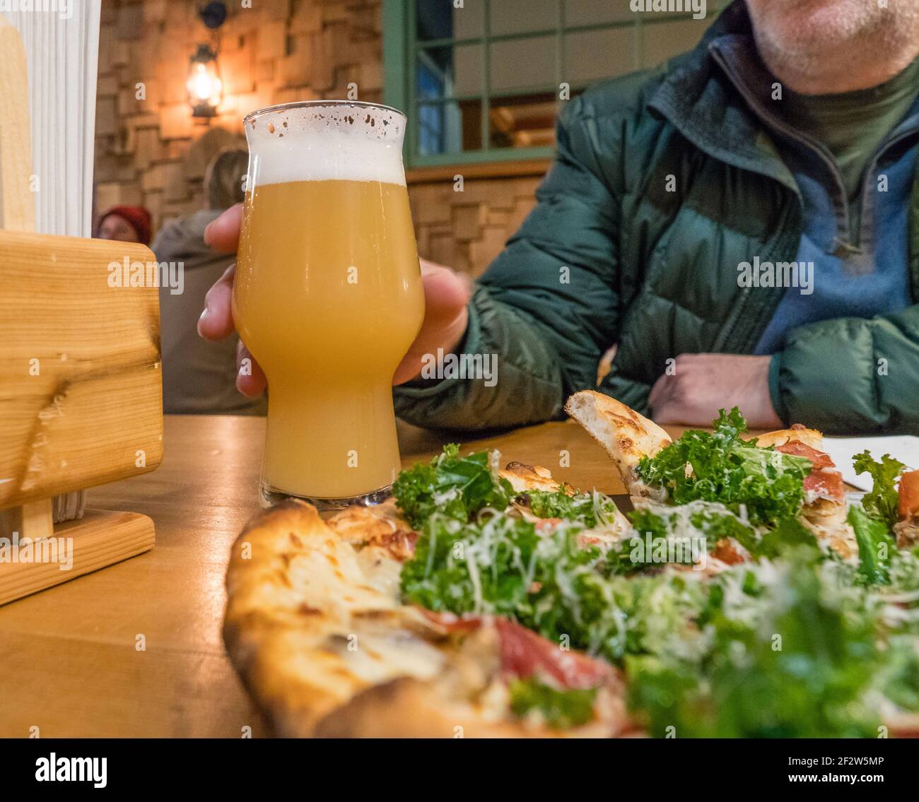 Mann im Hintergrund hält ein großes Glas blasses Bier mit einer großen Pizza vor sich. Stockfoto