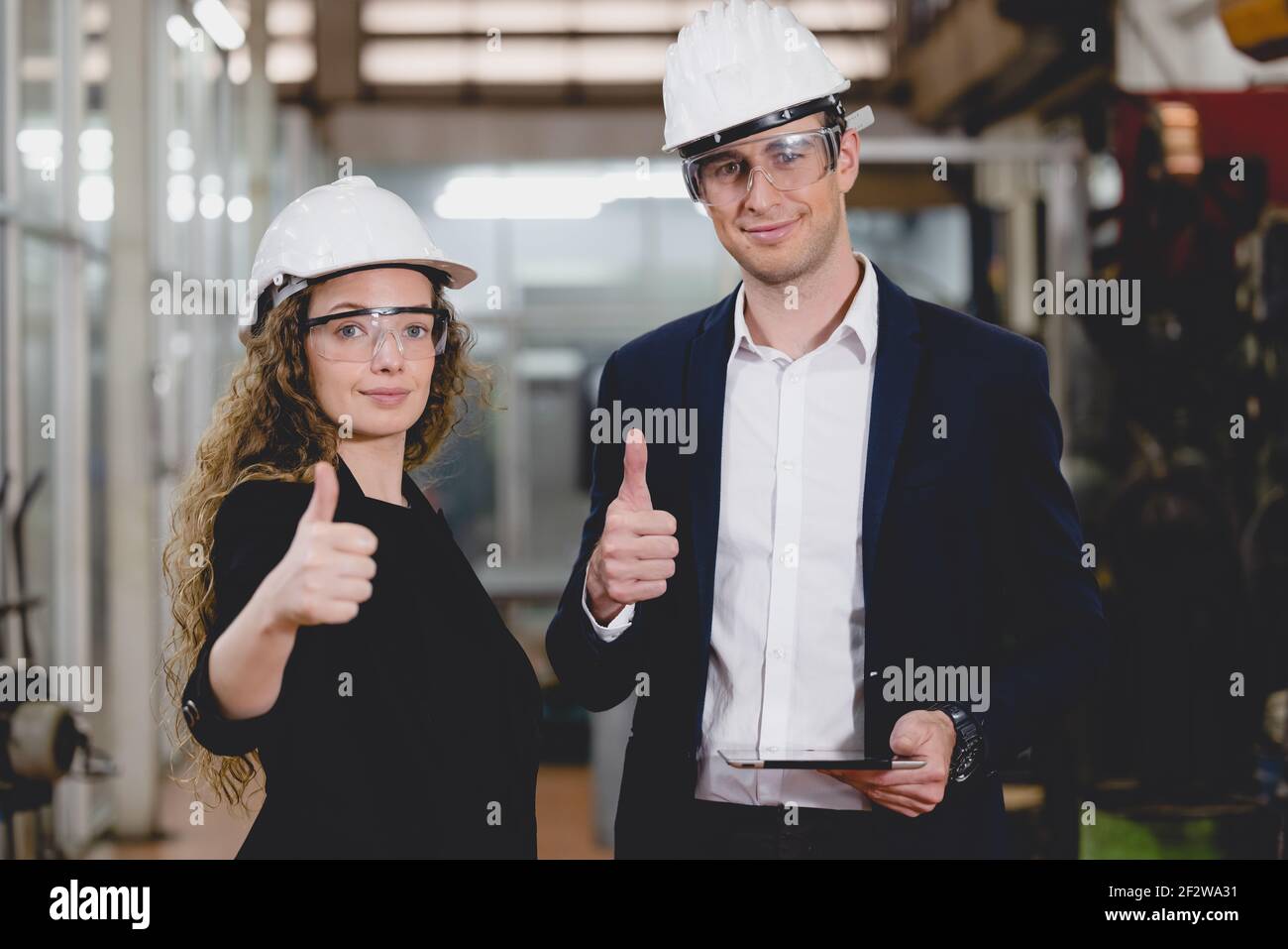 Portrait von zwei Machinists steht mit selbstbewusst mit Schutzhelm vor der Glaswand der Industriefabrik. Stockfoto