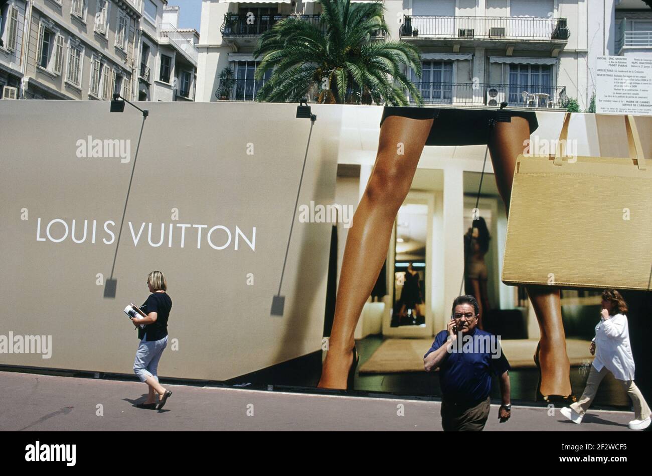 Mann, der unter den überlebensgroßen Beinen einer Louis Vuitton Werbung läuft. Stockfoto