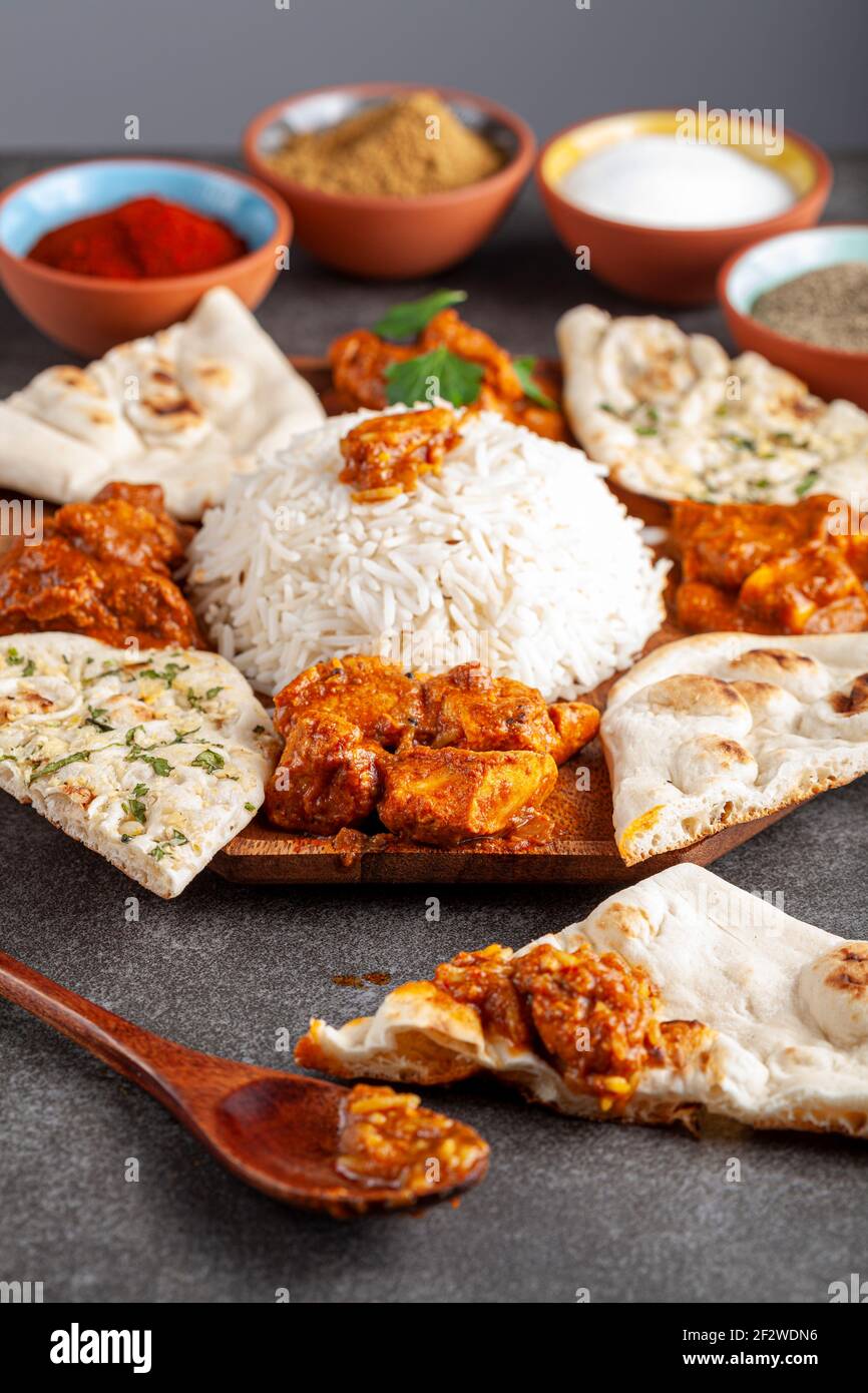 Angewinkeltes Bild einer Gourmet-Mischung aus indischen Gerichten wie Reis, Naan, Tikka Masala, Butterhuhn und Curry. Gewürze und Kräuter sind in verschwommen gesehen Stockfoto