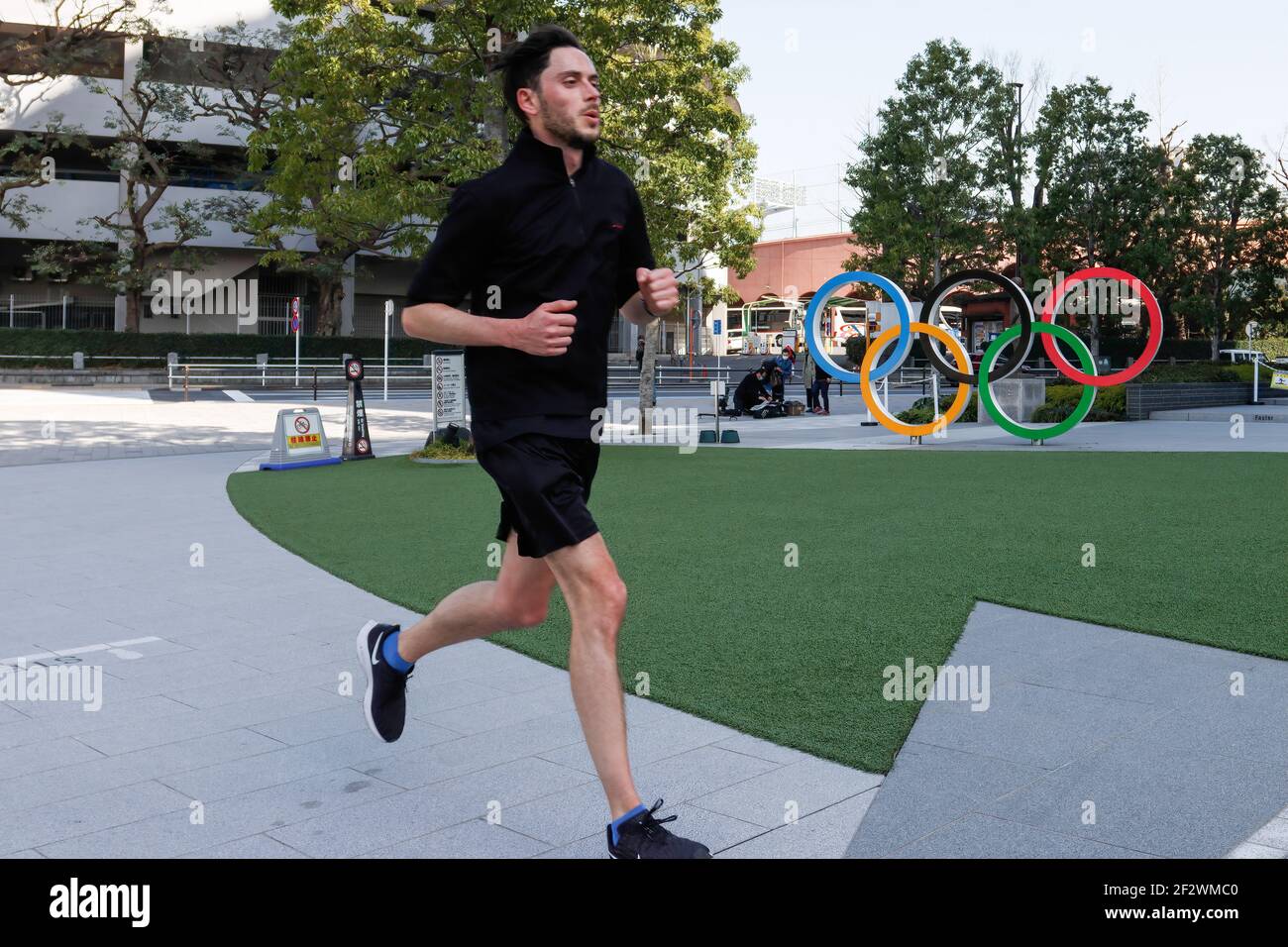 Tokio, Japan. März 2021, 11th. Ein Mann joggt an den olympischen Symbolen der fünf verschachtelten Ringe vorbei, die in der Nähe des Nationalstadions in Tokio abgebildet sind. Etwa 80% der Japaner in den letzten Umfragen sagen, dass die Olympischen Spiele verschoben oder abgesagt werden sollten, und fast so viele wollen keine Fans aus dem Ausland. Kredit: SOPA Images Limited/Alamy Live Nachrichten Stockfoto