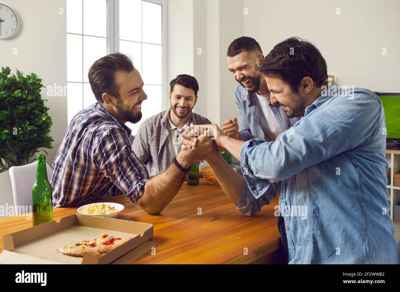 Fröhliche Gesellschaft von männlichen Freunden zu Hause Bier trinken und im Wettbewerb in Arm Wrestling. Stockfoto