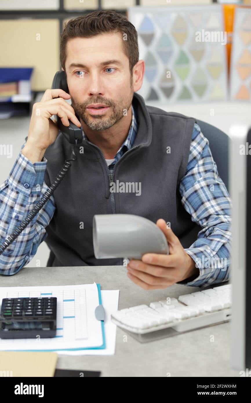 Arbeiter am Telefon hält sanitäre Abflussrohre in der Werkstatt Stockfoto