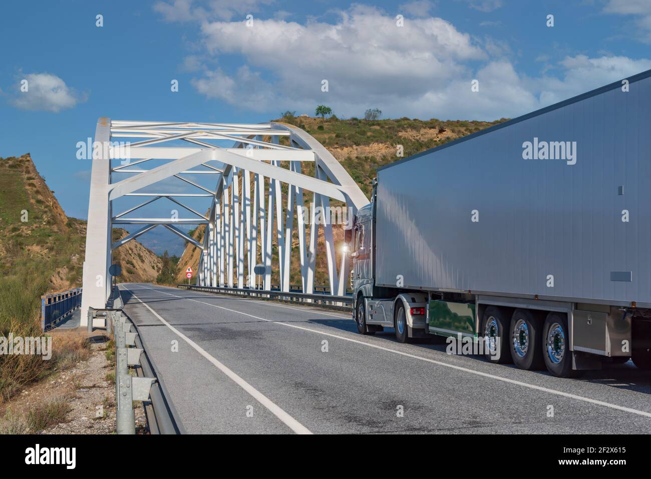 LKW mit gekühltem Sattelauflieger auf einer Bergstraße und über eine Eisenbrücke. Stockfoto