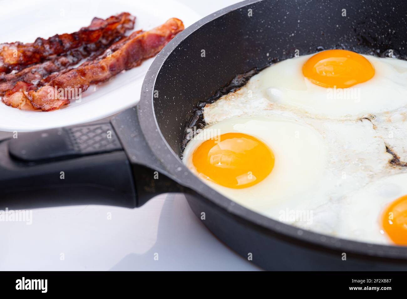 Spiegeleier und Speck in einer Pfanne oder Pfanne kochen. Idee für das Frühstück am Morgen. Gelbe Eigelb Eier und gebratene Scheiben Speck Stockfoto