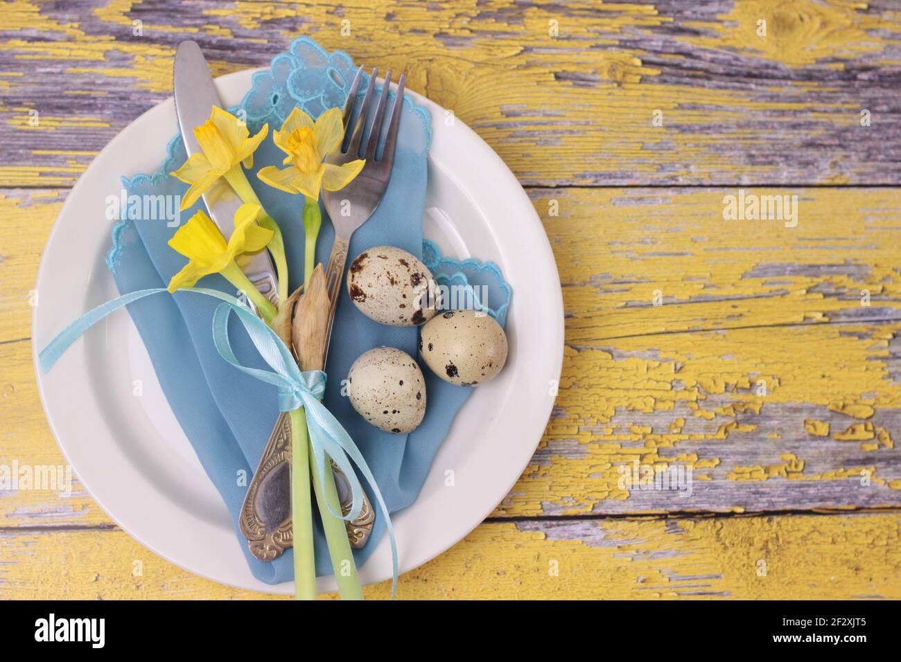 Schöne Osterfeiertage Tischausstattung mit Besteck auf Scheunenbrettern.Narzissen, Wachteleier, Essgeschirr mit Schleife auf türkisfarbener Serviette und weißem Teller Stockfoto