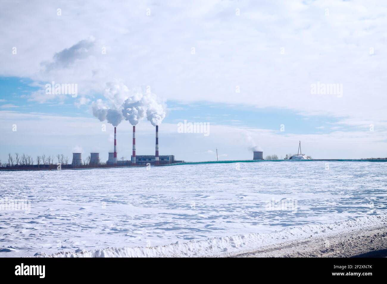 Rauchende Schornsteine einer Fabrik auf einem Hintergrund aus Blau Himmel mit Wolken und weißem Schnee Stockfoto