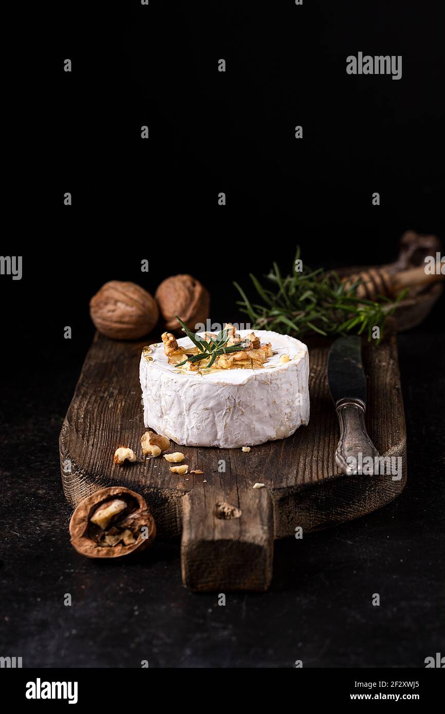 Köstlicher Gourmet Camembert Käse garniert mit Walnüssen und frischem Rosmarin Serviert auf rustikalem Holzbrett Stockfoto