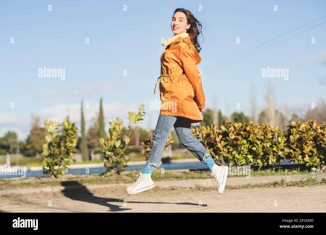 Seitenansicht von weiblichen Teenager in Freizeitkleidung Blick auf Kamera beim Springen gegen gewellten Fluss und blauen Himmel Stockfoto