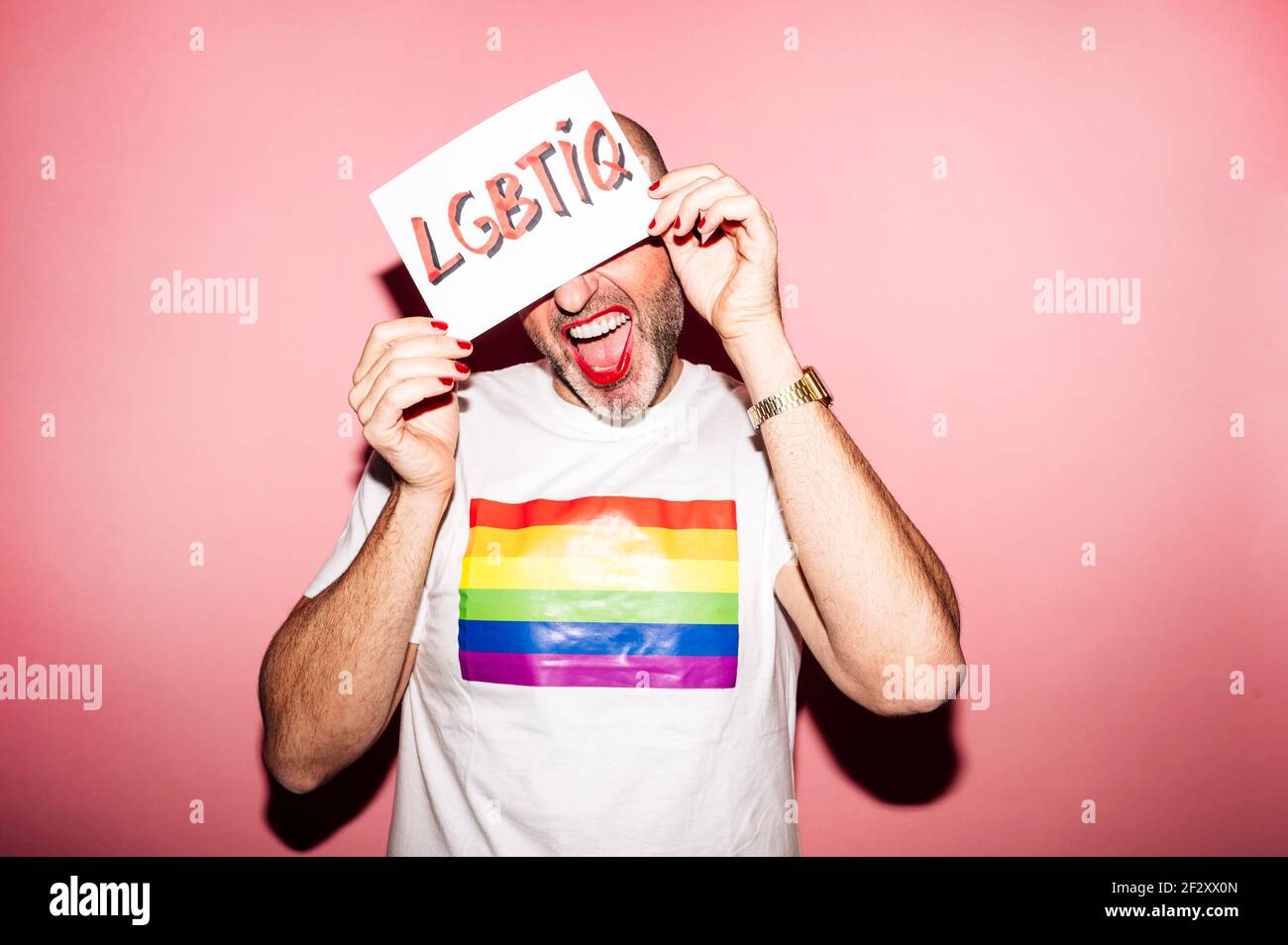 Crop rebellischen bärtigen homosexuellen Mann mit roten Lippen und Maniküre Erstellen Grimasse beim Anzeigen und Bedecken Gesicht mit Papier mit LGBTIQ-Text gegen p Stockfoto