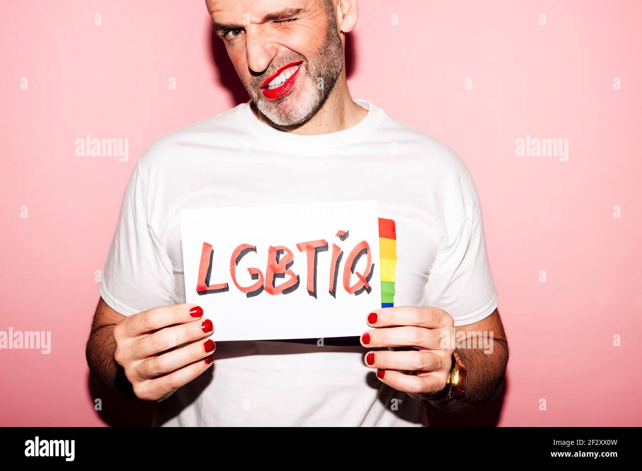 Crop rebellischen bärtigen homosexuellen Mann mit roten Lippen und Maniküre Erstellen von Grimasse beim Anzeigen von Papier mit LGBTIQ-Text gegen Rosa Hintergrund Stockfoto