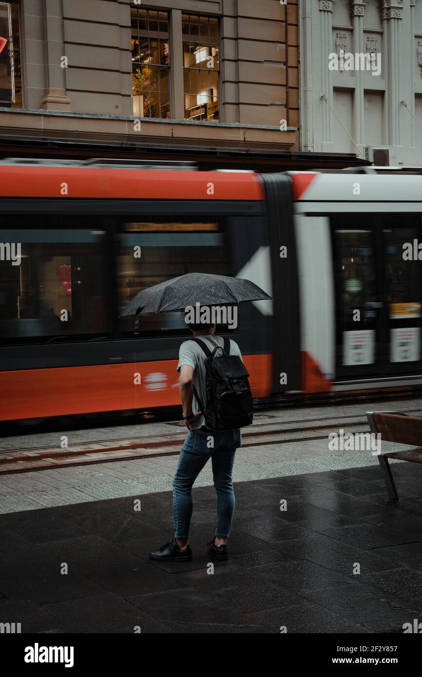 Mann mit Regenschirm und Tasche wartet darauf, die George Street in Sydneys CBD zu überqueren. Stockfoto