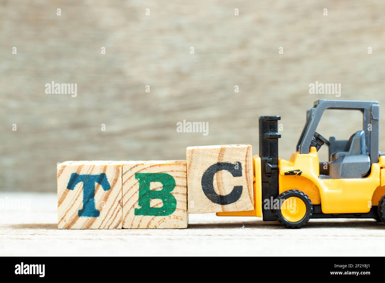 Spielzeug Gabelstapler halten Buchstabenblock c, um Wort TBC abzuschließen (Abkürzung von muss bestätigt oder fortgesetzt werden) auf Holzhintergrund Stockfoto
