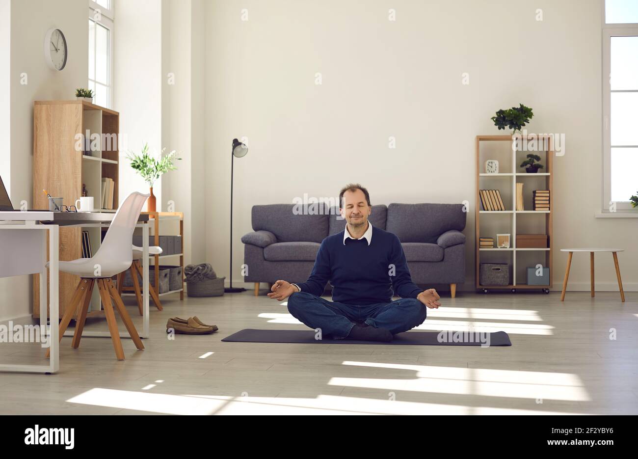 Entspannter reifer Mann meditiert in Lotuspose auf Yogamatte Auf der Büroetage Stockfoto