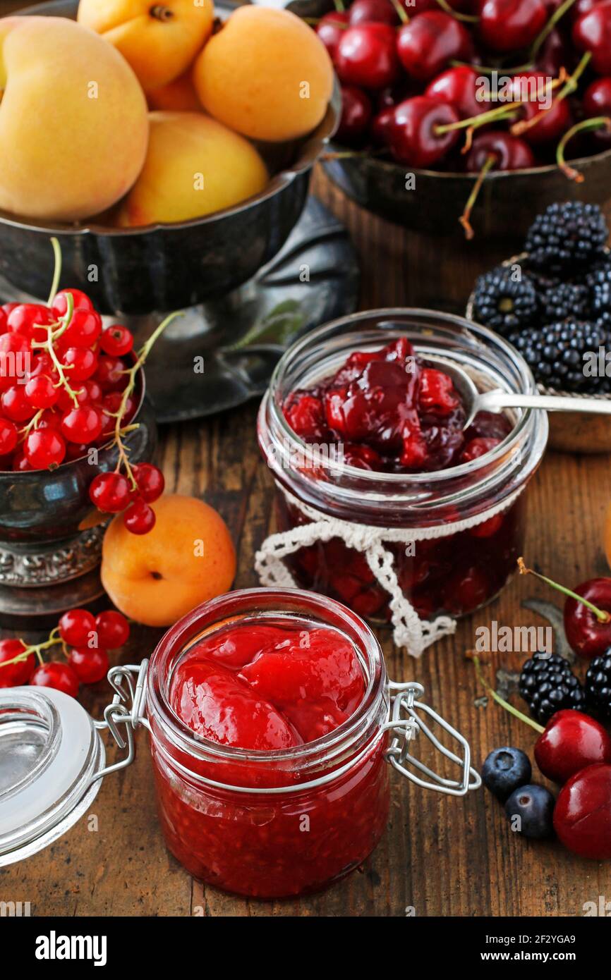 Gläser Kirschkerne Erdbeermarmelade zwischen Sommer und Herbst Früchte auf einem Holztisch. Stockfoto