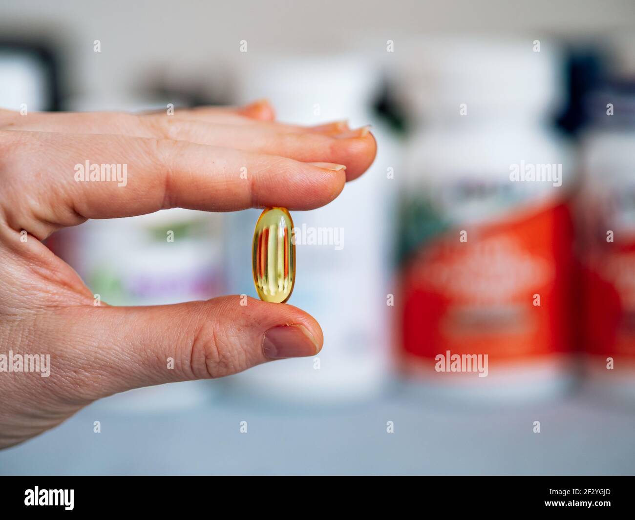 Vitamin D3, Omega oder Nachtkerzenöl Gelkapsel in weiblicher Hand auf verschwommene Nahrungsergänzungsmittel Gläser Hintergrund. Platz für Text kopieren. Stockfoto