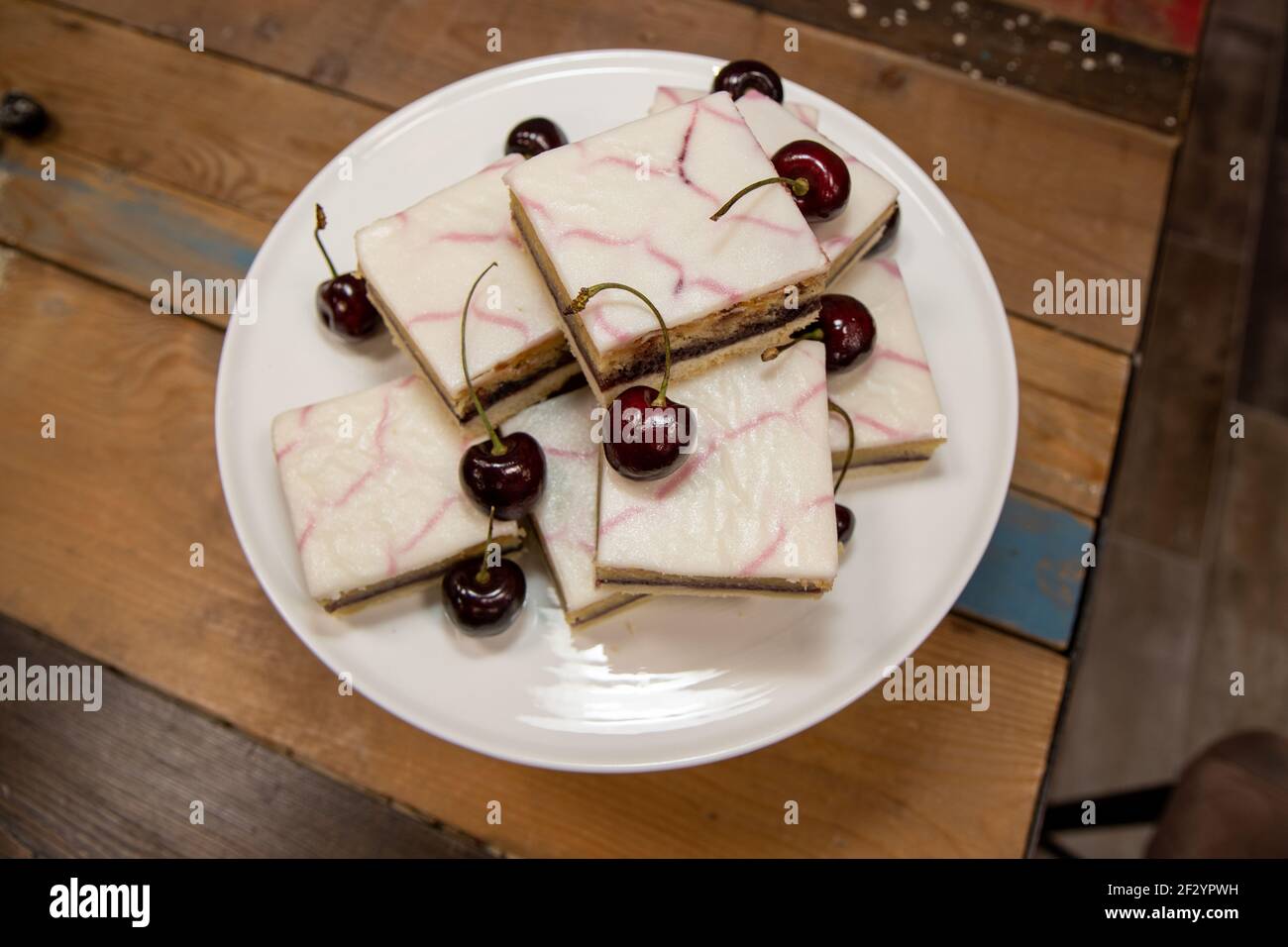 Ein köstlicher Teller von Cherry Bakewell Quadrate Törtchen auf einem Küchentisch aus Holz, umgeben von Kirschen Stockfoto